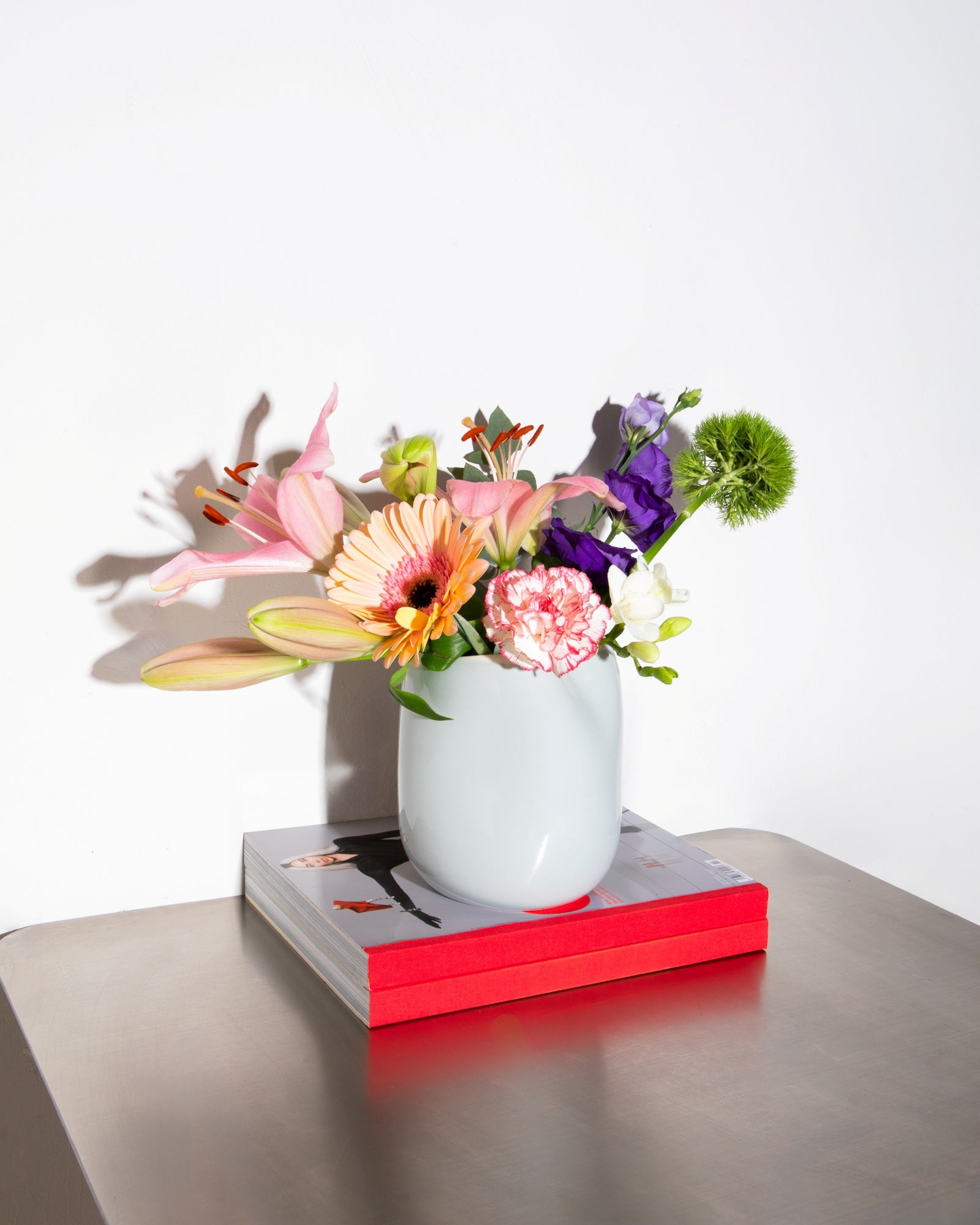 Bunter Blumenstrauß in weißer Vase auf rot umrandetem Buch, stilvoll auf einem Tisch platziert.