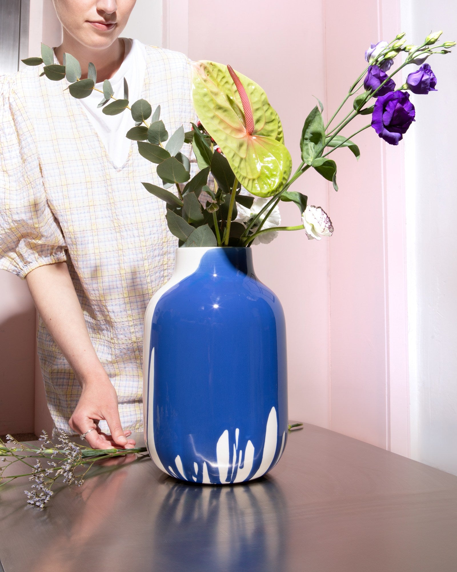 Person neben einer großen blauen Vase mit buntem Blumenstrauß auf einem Tisch.