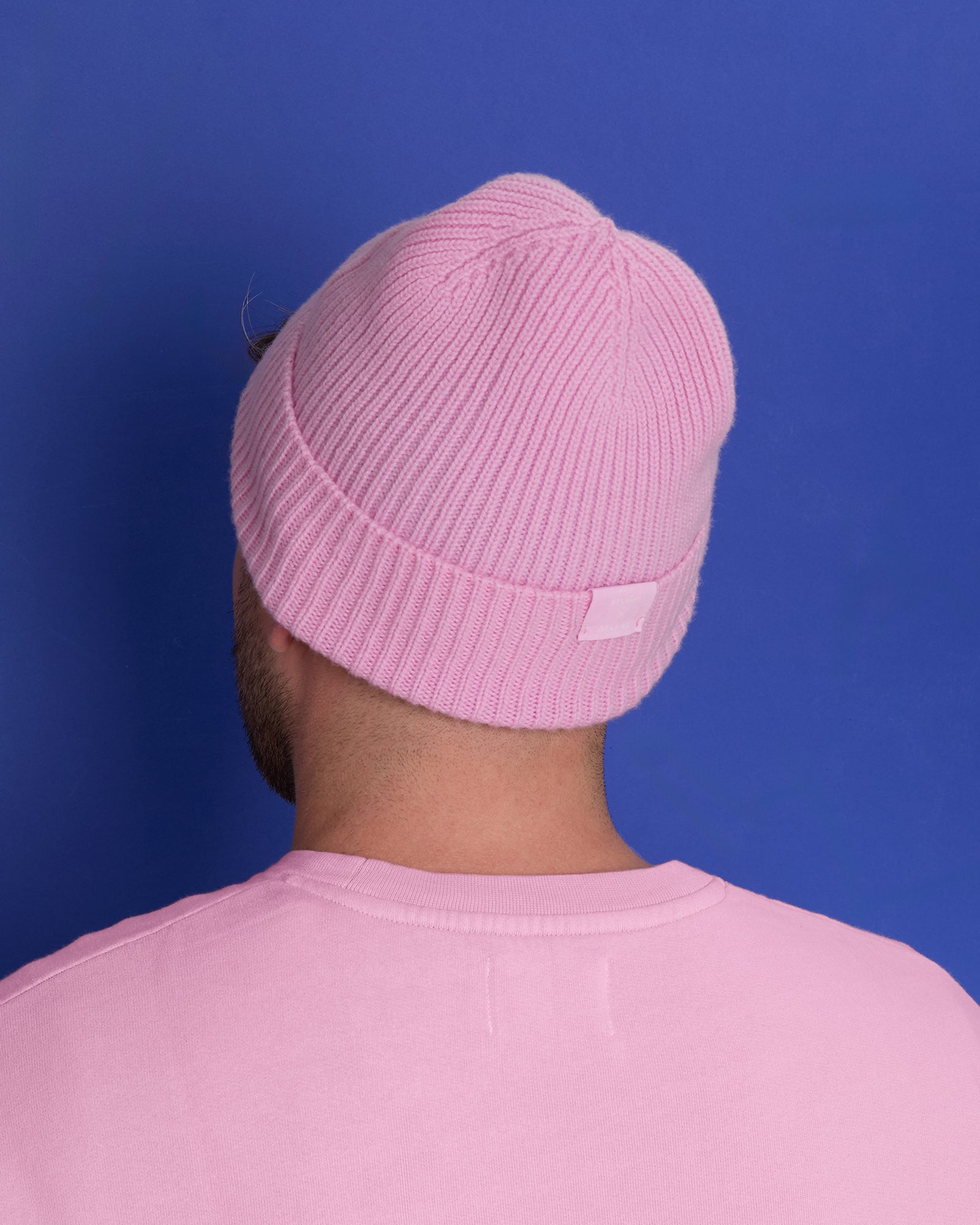 Person mit rosa Mütze und Shirt vor blauem Hintergrund, von hinten.