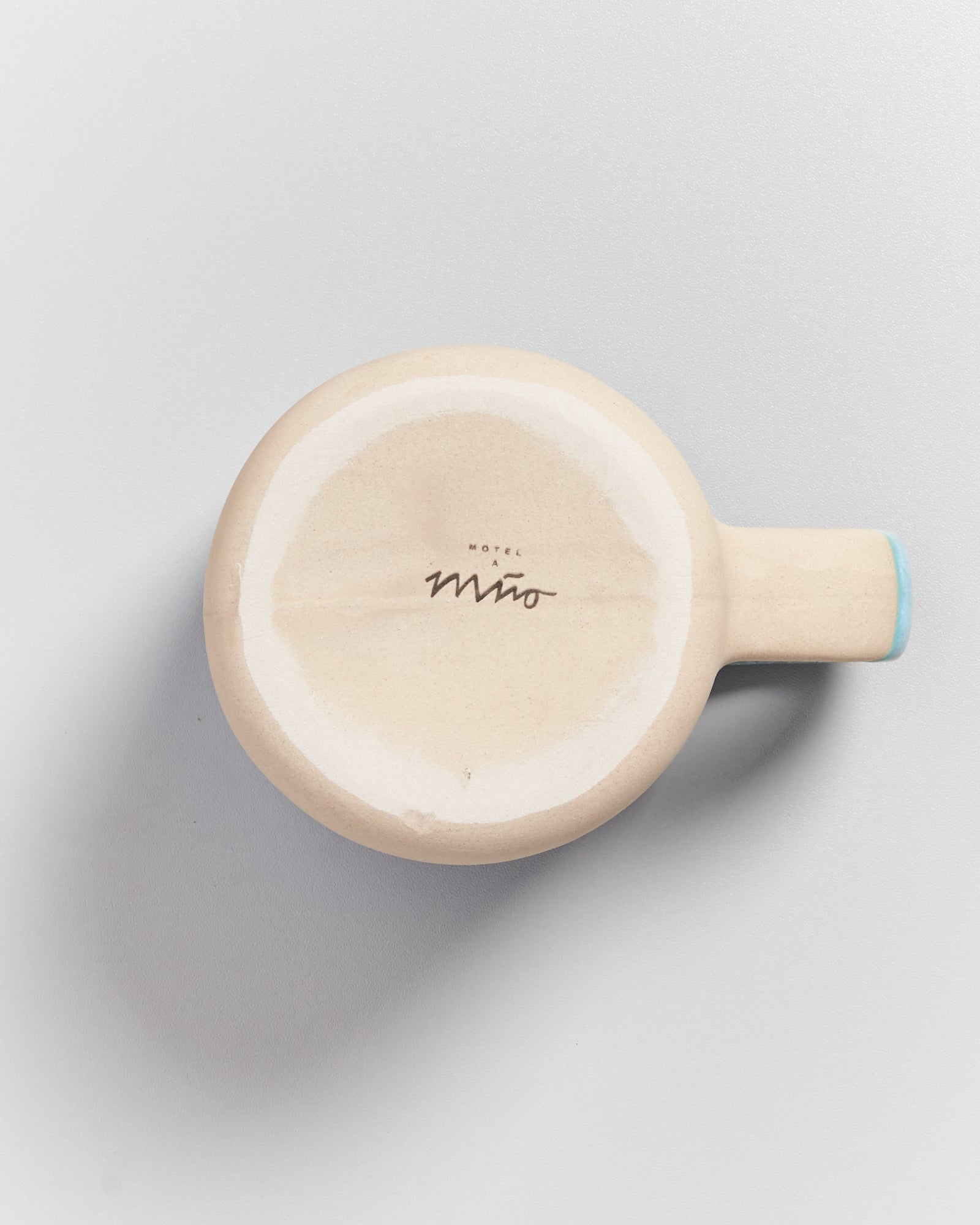 Beige runder Keramikbehälter mit seitlichem Griff auf weißem Hintergrund, beschriftet mit "Motel a Mio".