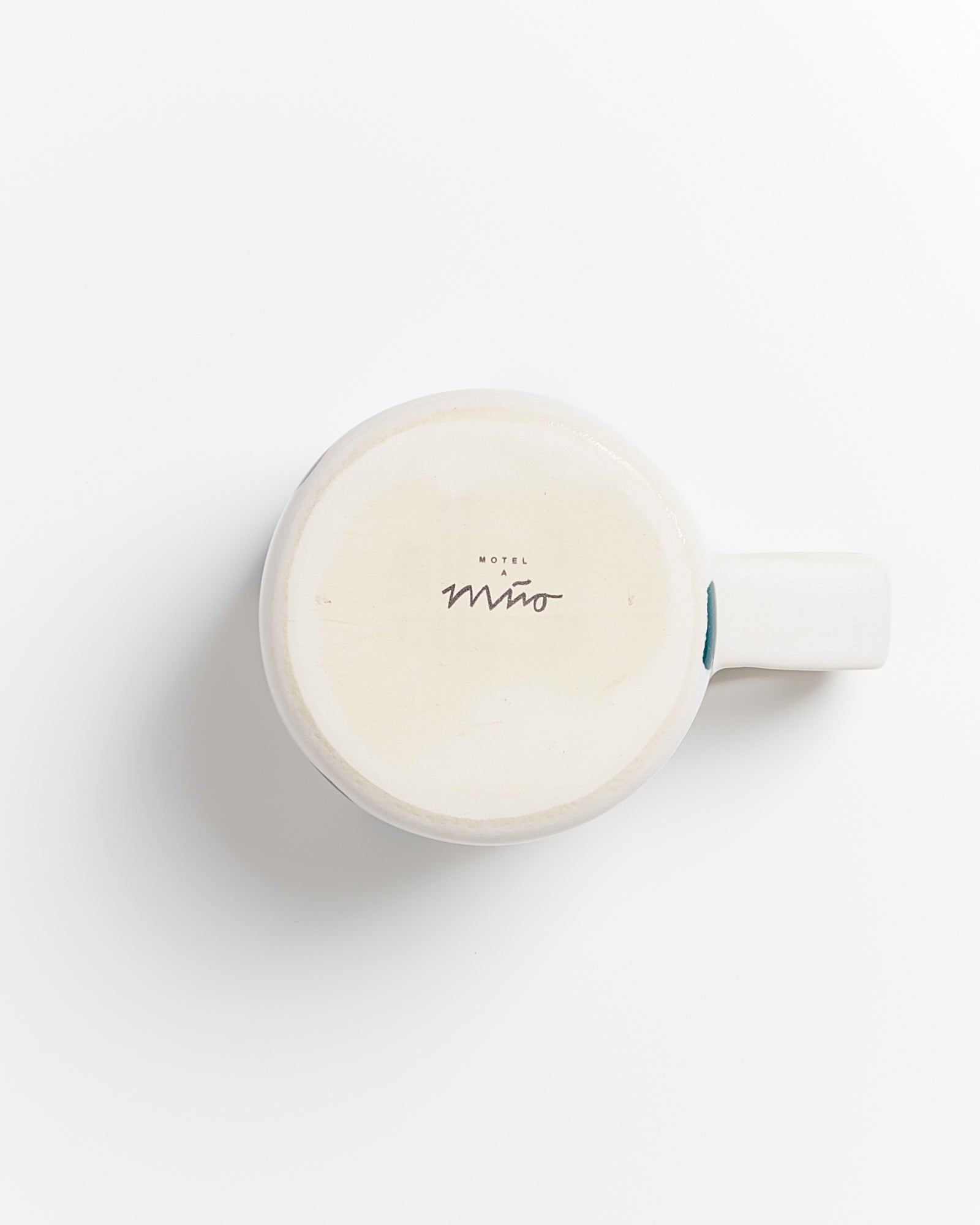 Weiße Tasse, die auf der Unterseite liegend das Wort "Motel Mio" zeigt, auf weißem Hintergrund.
