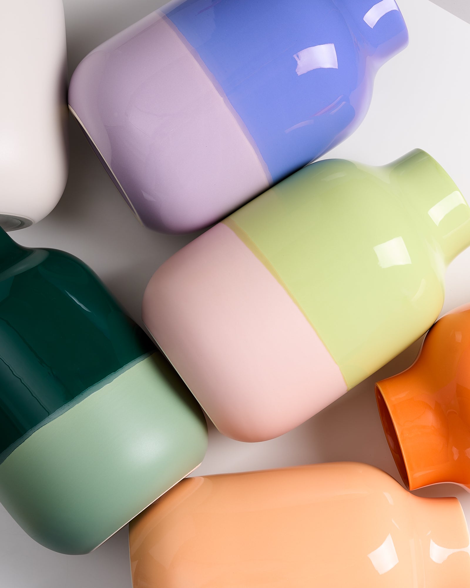 Mehrere bunte Vasen in Pastellfarben liegen auf einer weißen Oberfläche.