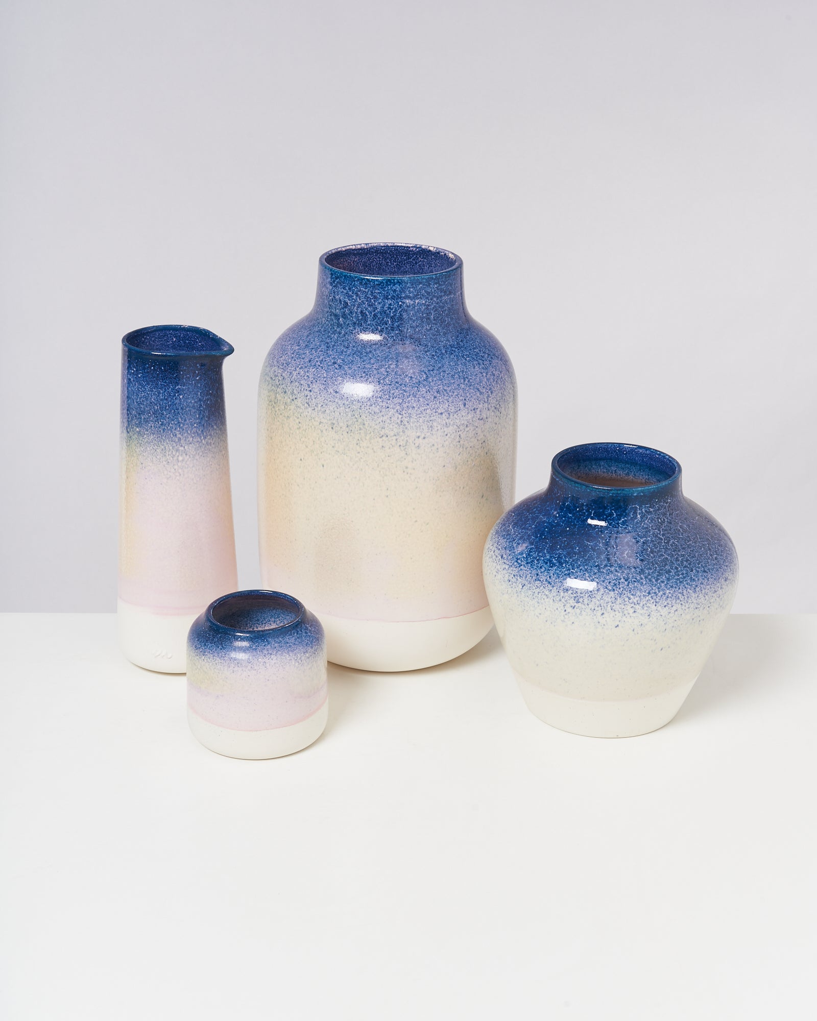 Vier Keramikwaren in verschiedenen Formen und Größen mit blau-weißem Farbverlauf stehen auf einem weißen Tisch.