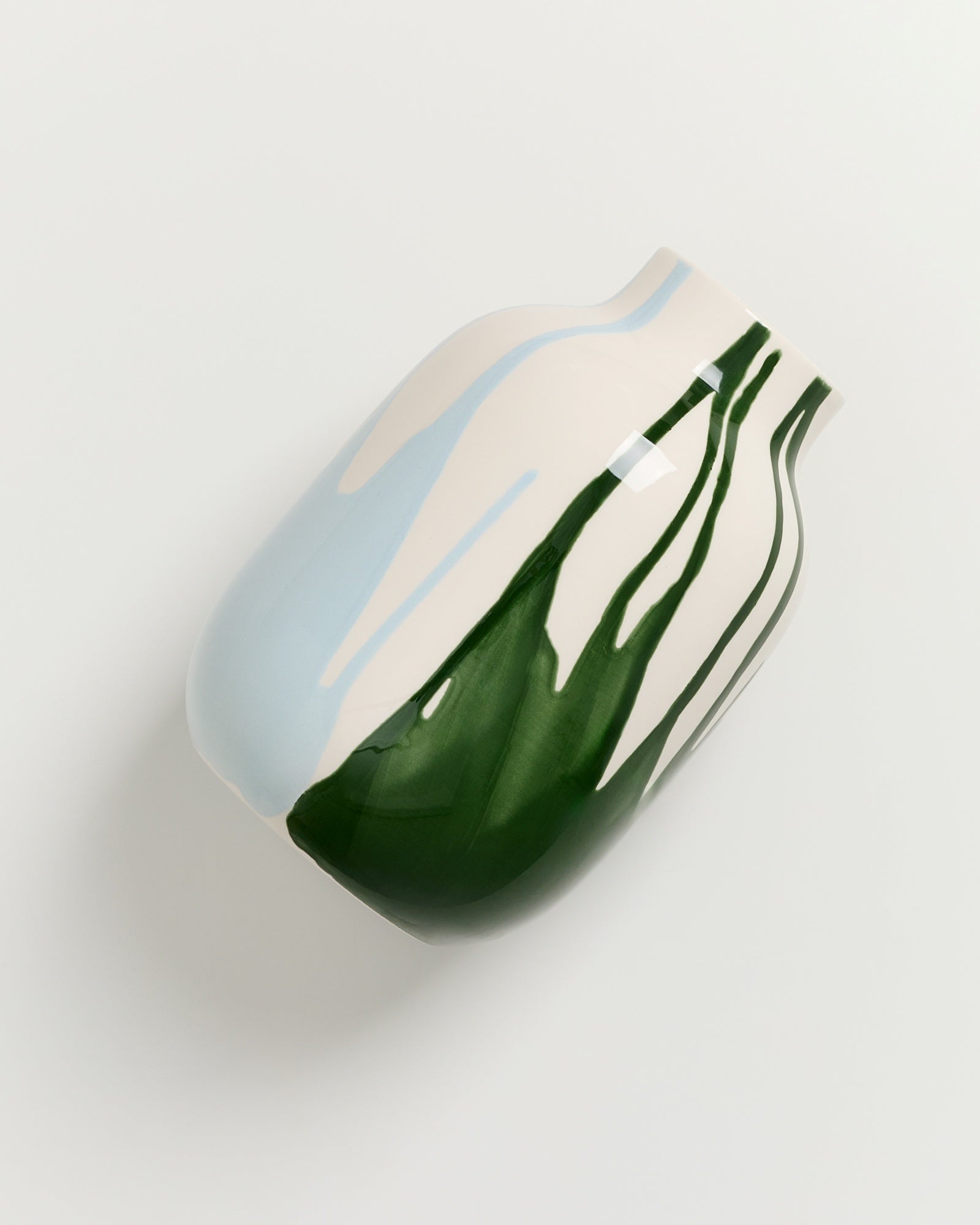 Keramikvase mit blau-grünem abstraktem Streifenmuster auf weißem Hintergrund.