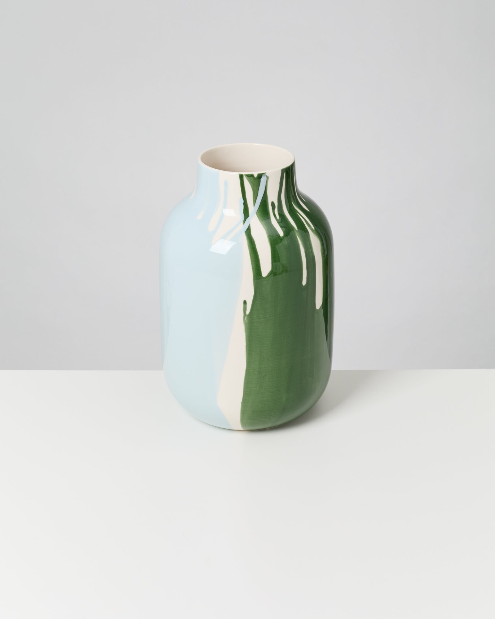 Keramikvase mit grünem und blauem Tropfmuster auf weißem Hintergrund.
