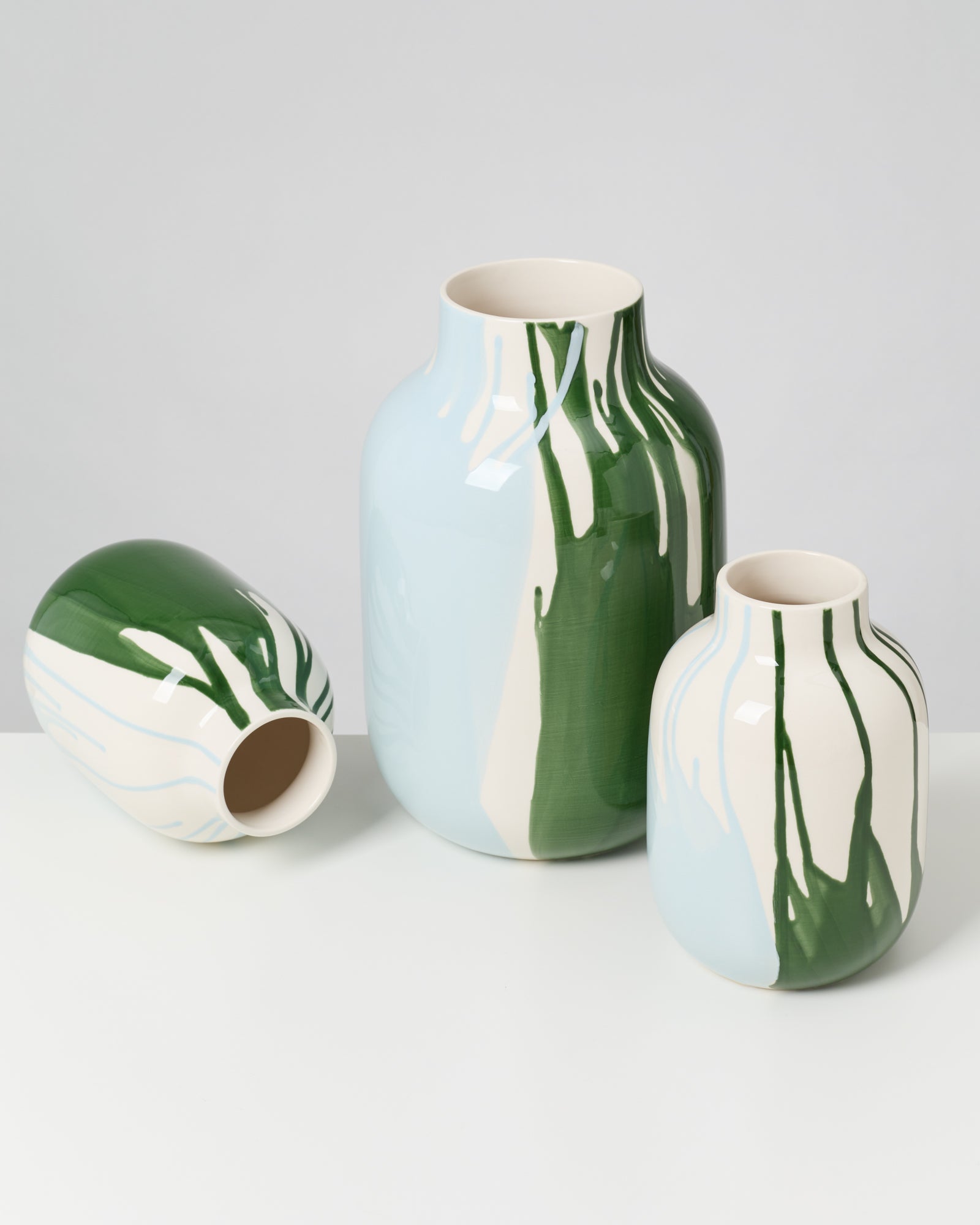 Drei bemalte Vasen in verschiedenen Größen, mit grünen, blauen und weißen Mustern, auf einem weißen Tisch.