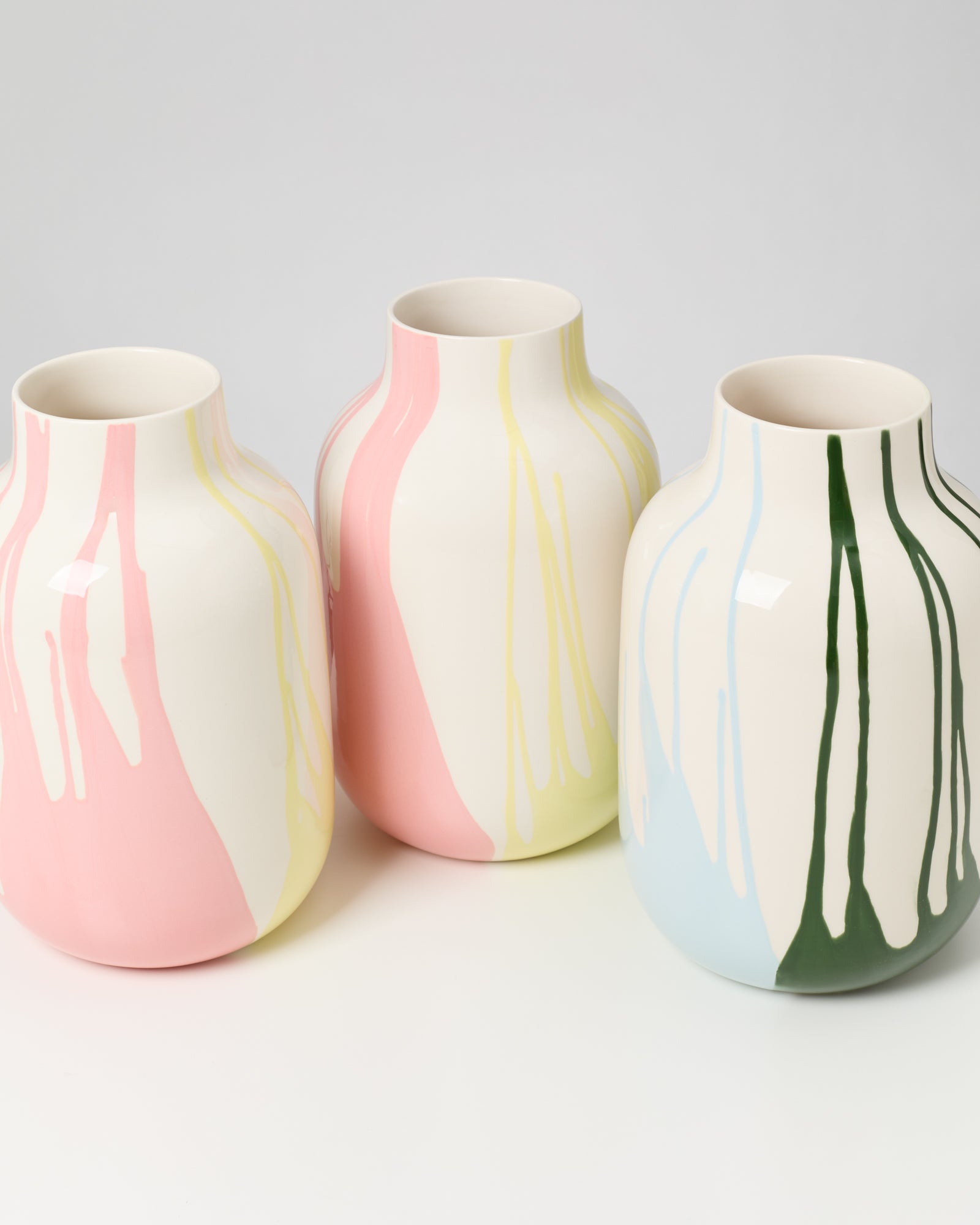Drei bauchige Vasen mit bunten, verlaufenden Streifen in Rosa, Gelb, Blau und Grün auf weißem Hintergrund.