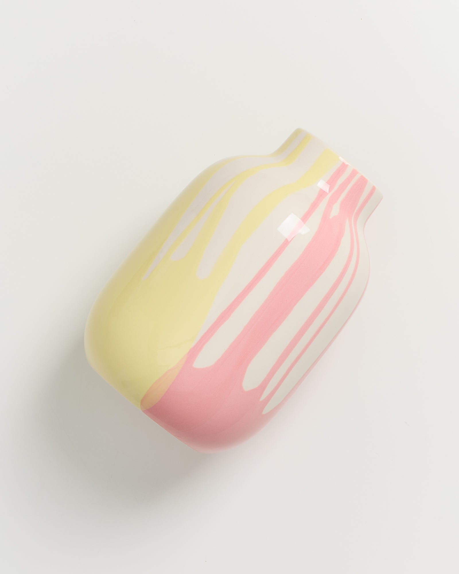 Vase mit gelben und rosa Rinnmustern auf hellem Hintergrund, von oben fotografiert.