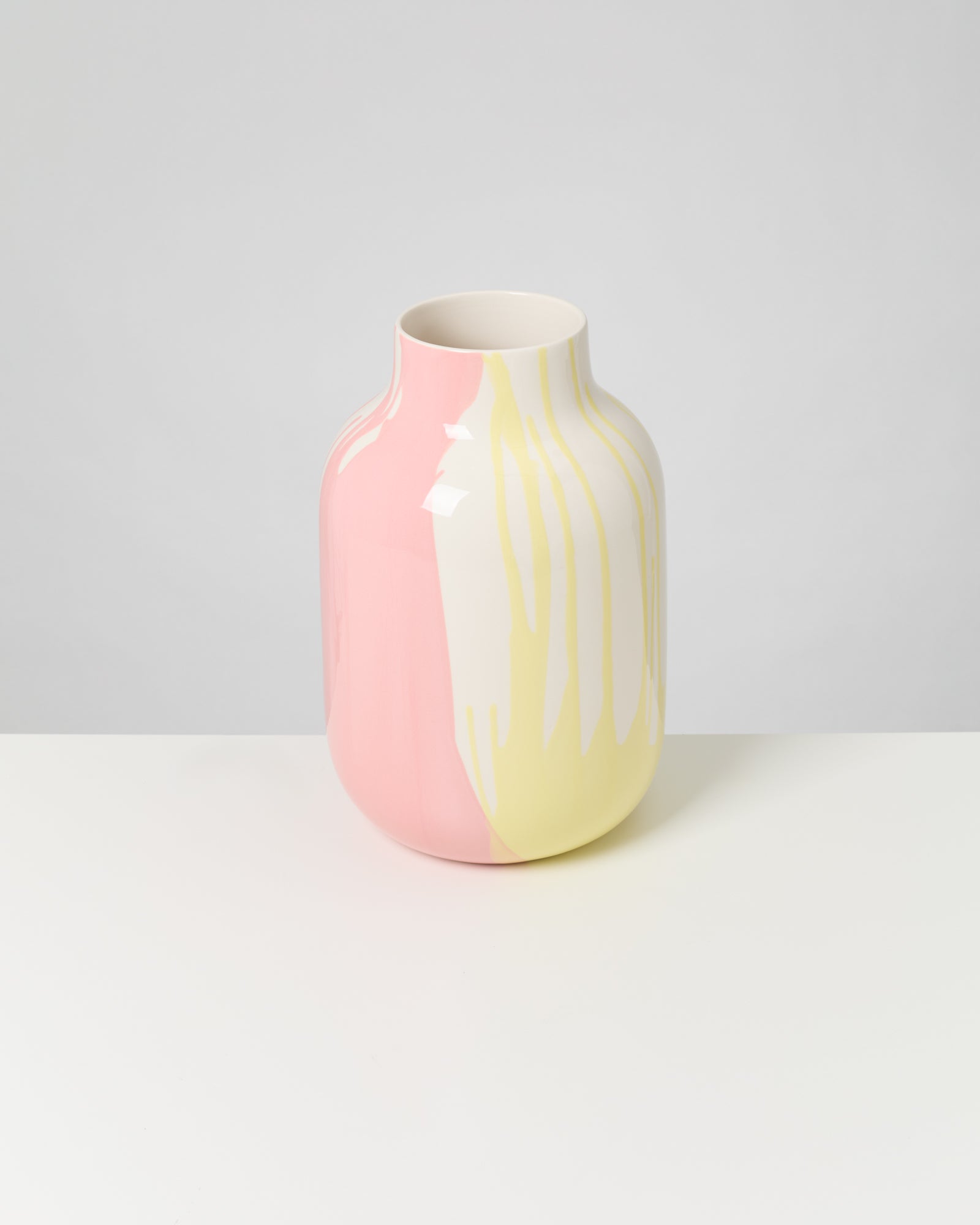 Große Vase mit rosa, gelber und weißer Marmorierung steht auf einem weißen Tisch vor grauem Hintergrund.