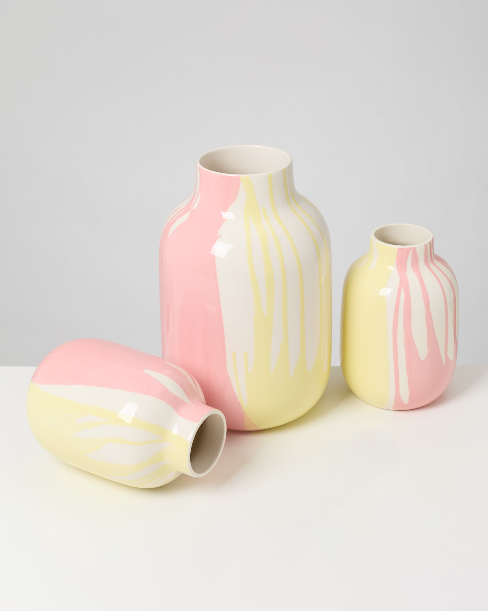 Drei Vasen in Pastellfarben Gelb, Rosa und Weiß in verschiedenen Größen auf weißem Hintergrund.