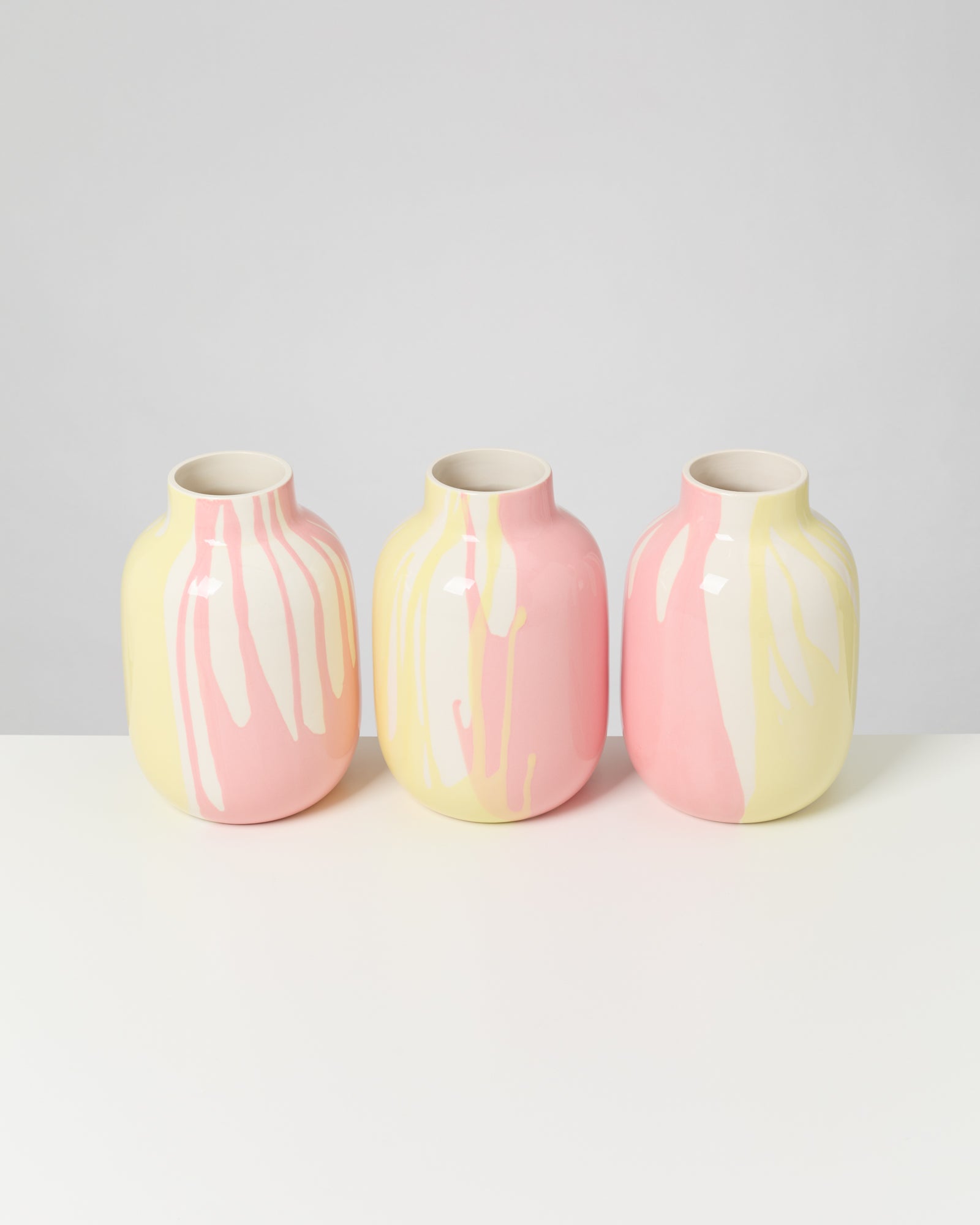 Drei Vasen mit rosa, gelben und weißen Streifen stehen nebeneinander auf einem weißen Tisch.