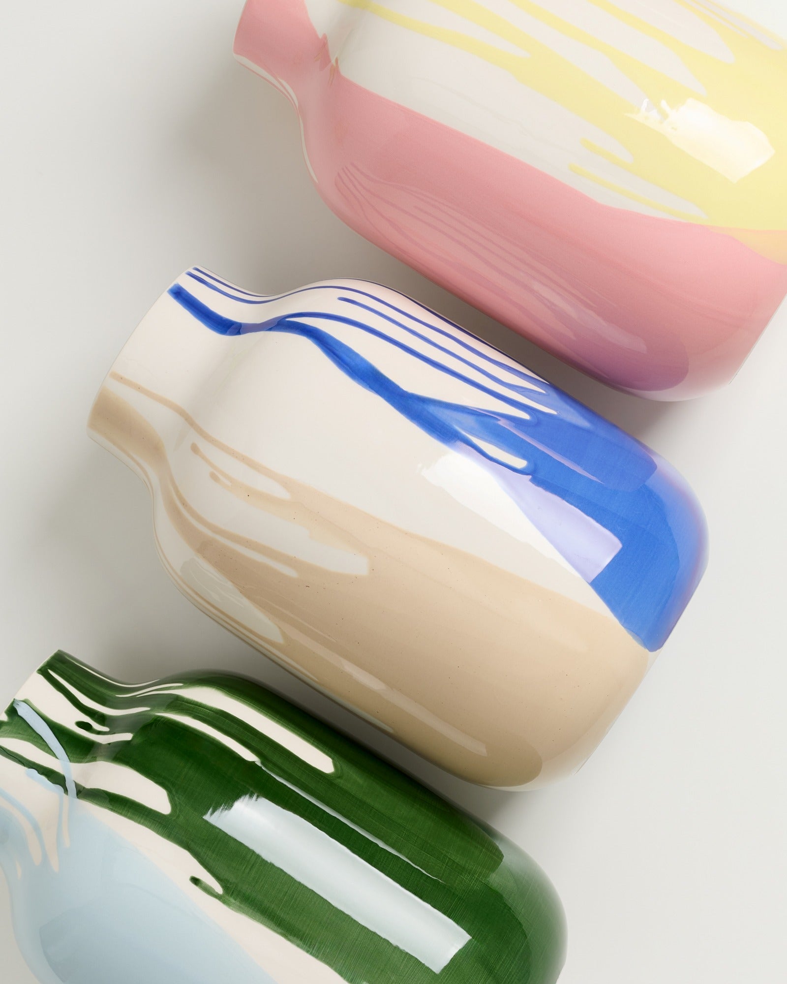 Drei bunte Keramikvasen in Pastelltönen, auf einem weißen Hintergrund von oben fotografiert.