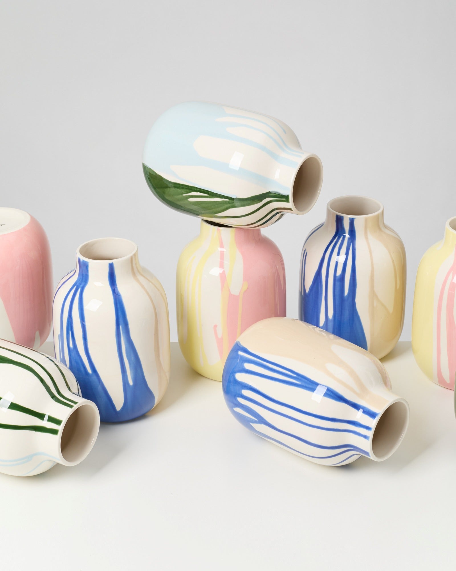 Mehrere bunte Keramikvasen mit farbigen Pinselstrichen stehen und liegen auf einem weißen Untergrund.