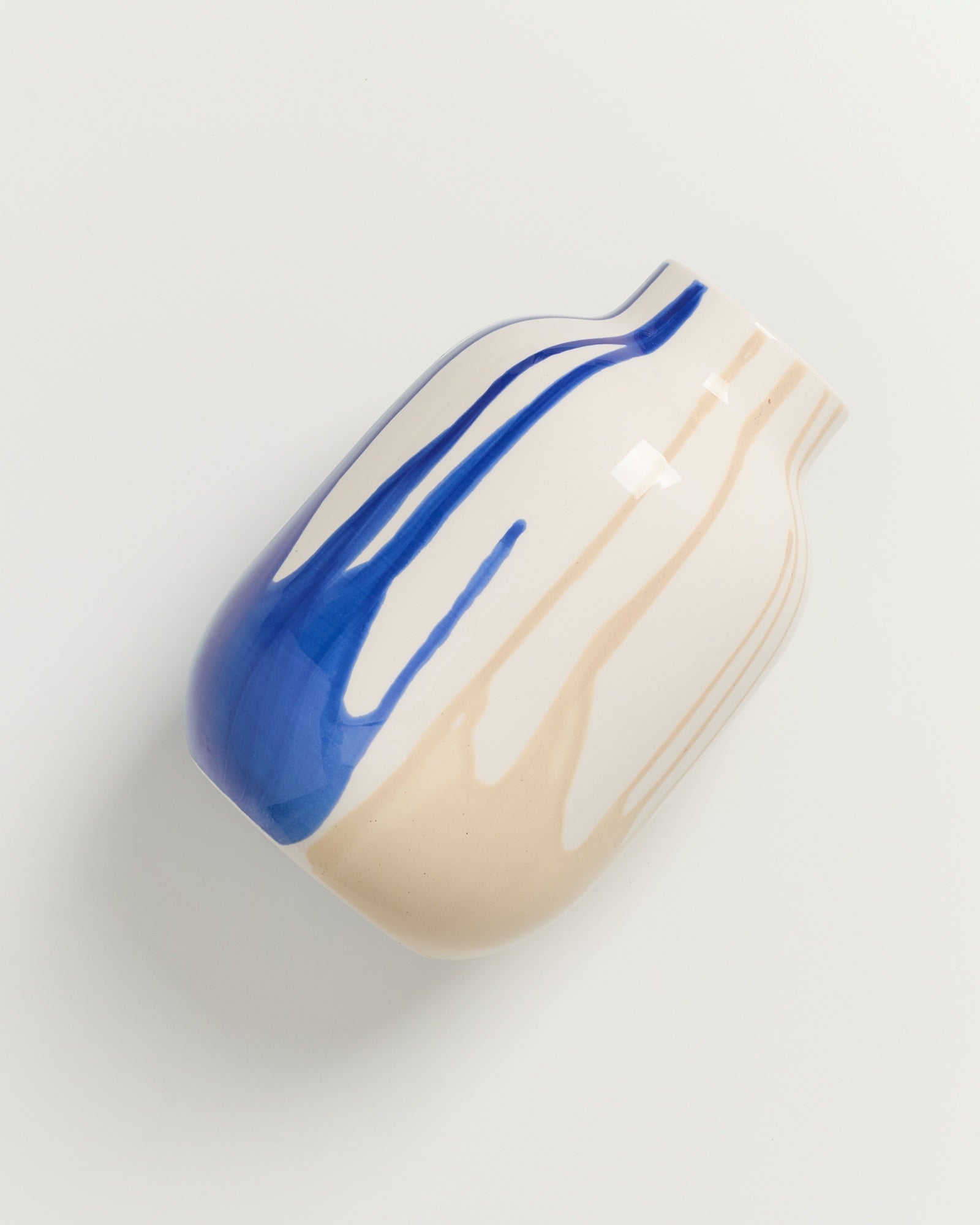 Keramikvase mit blauem und beigem Streifenmuster auf weißem Hintergrund.