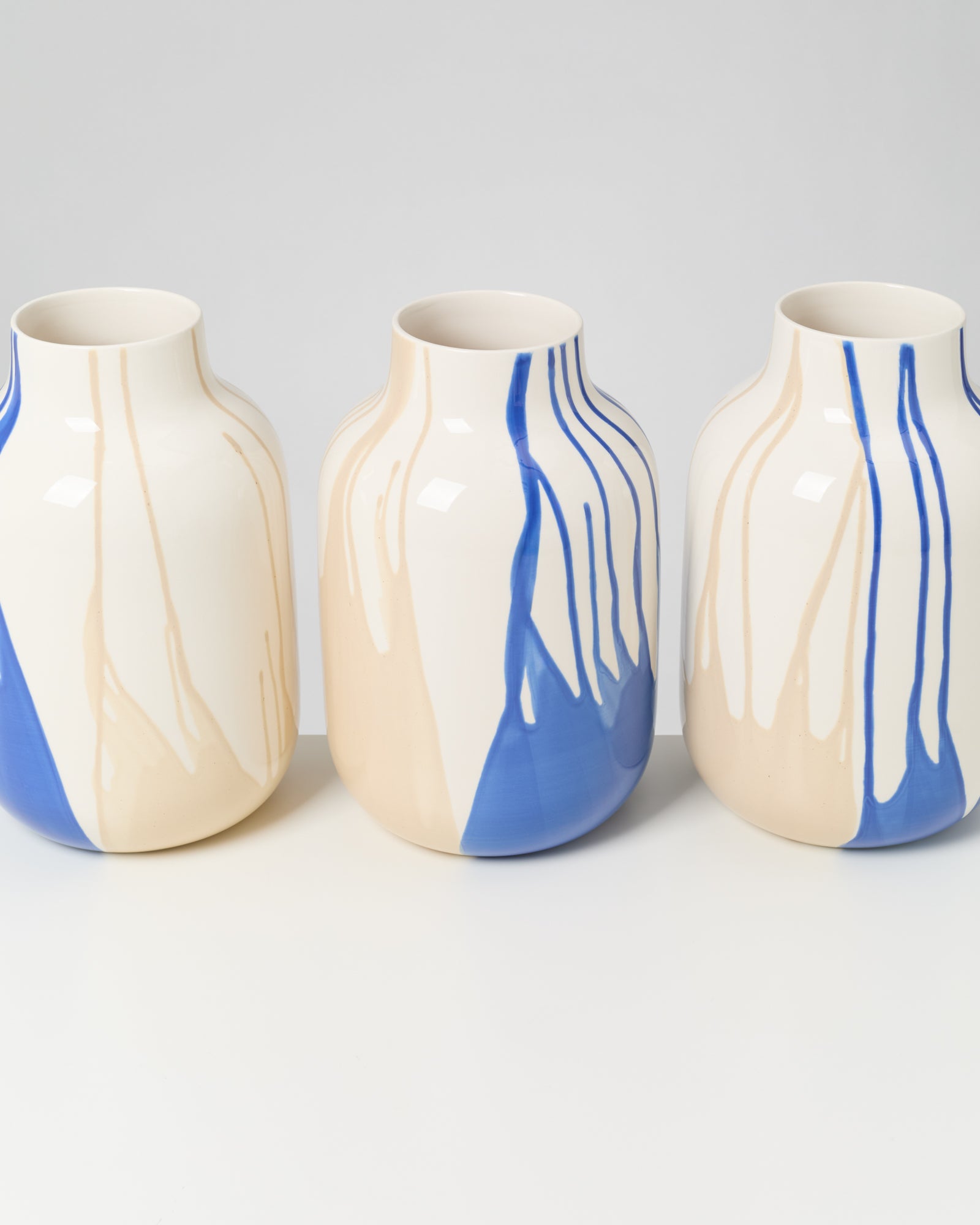 Drei Keramiken mit blau-beigen Streifen stehen nebeneinander auf einem weißen Hintergrund.