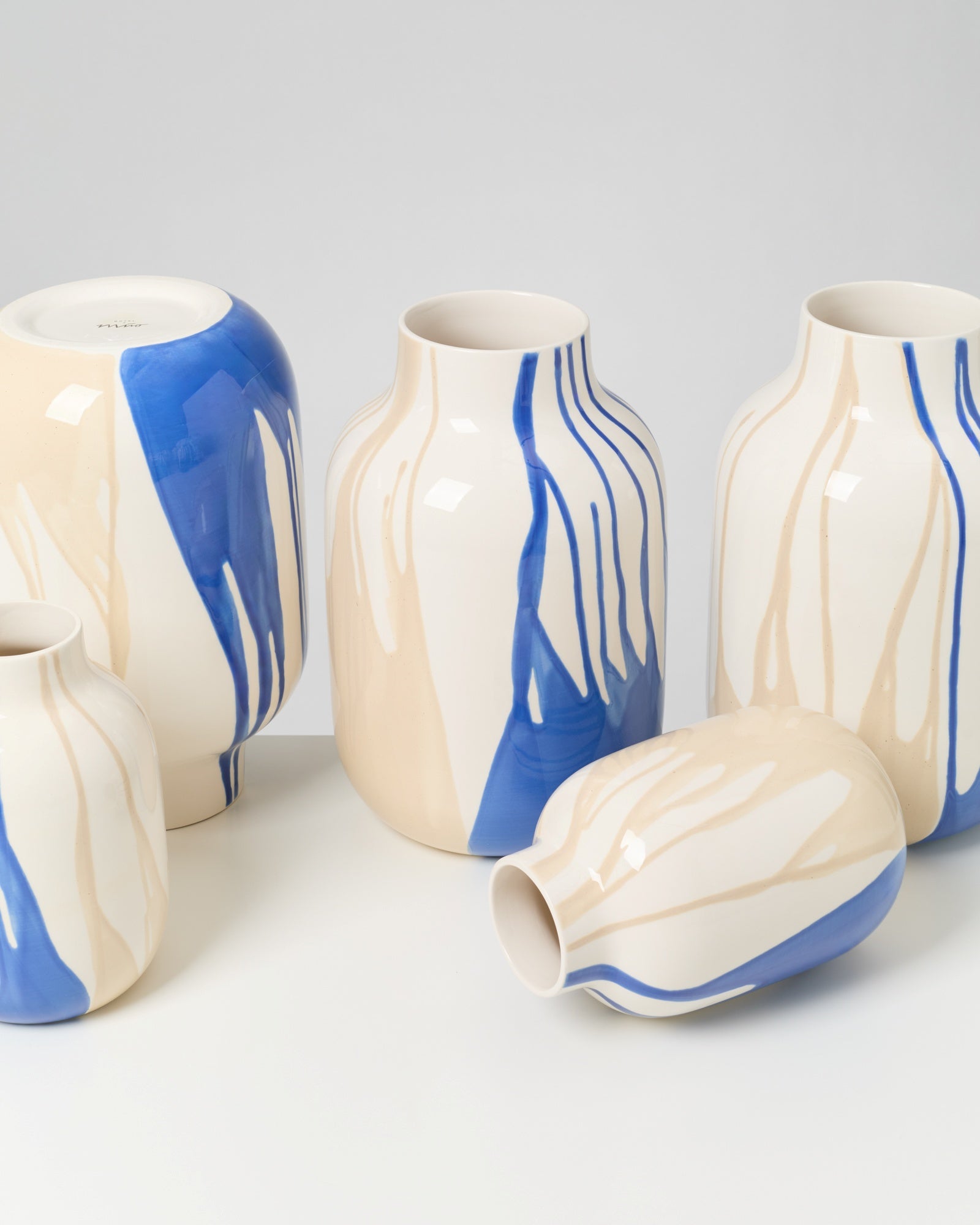 Fünf Keramikvasen mit blauen und beige-weißen Streifen auf weißem Hintergrund.