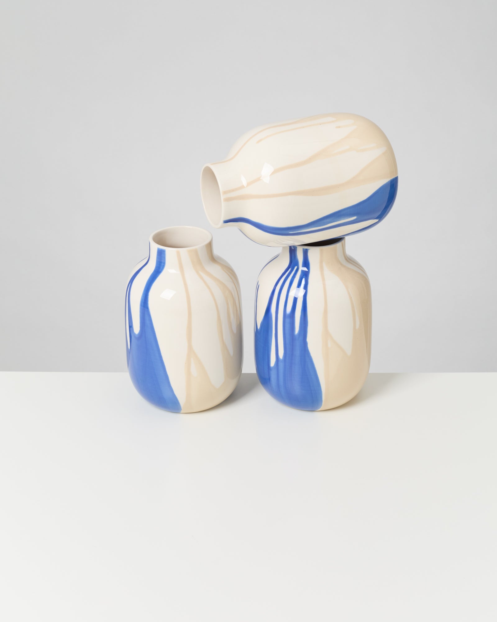 Drei cremefarbene Vasen mit blauem und beigem Muster stehen auf einem Tisch. Die obere Vase ist seitlich platziert.