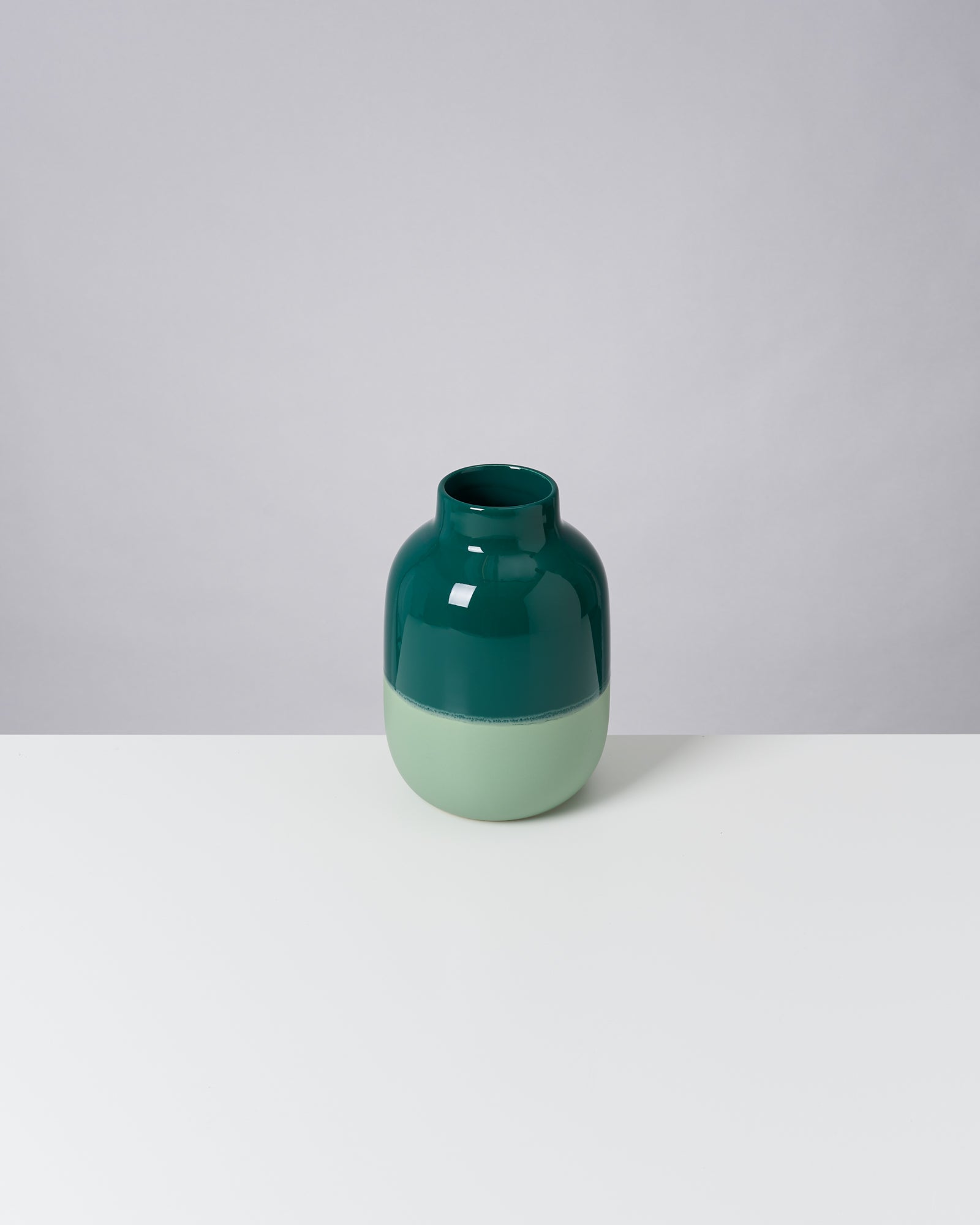 Grüne zweifarbige Vase auf weißem Tisch vor grauem Hintergrund.