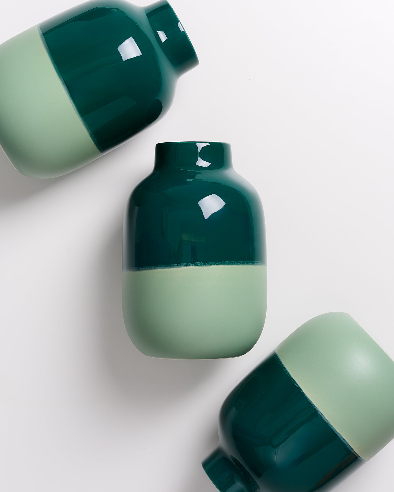 Drei grün-weiße Vasen auf weißem Hintergrund, in einer schrägen Anordnung zueinander.