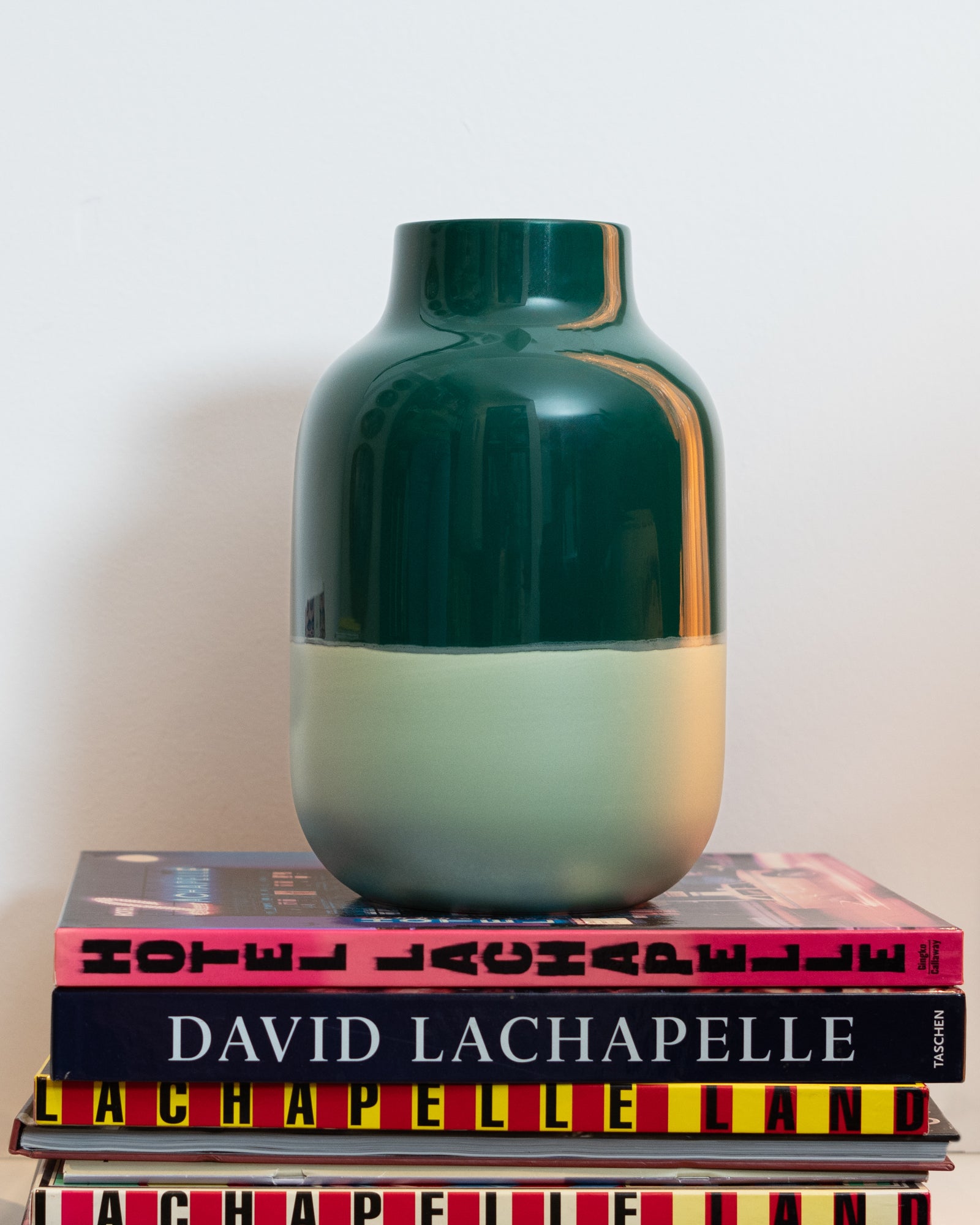 Grüne Vase steht auf einem Stapel Bücher, darunter Fotobände von David LaChapelle, vor einer weißen Wand.