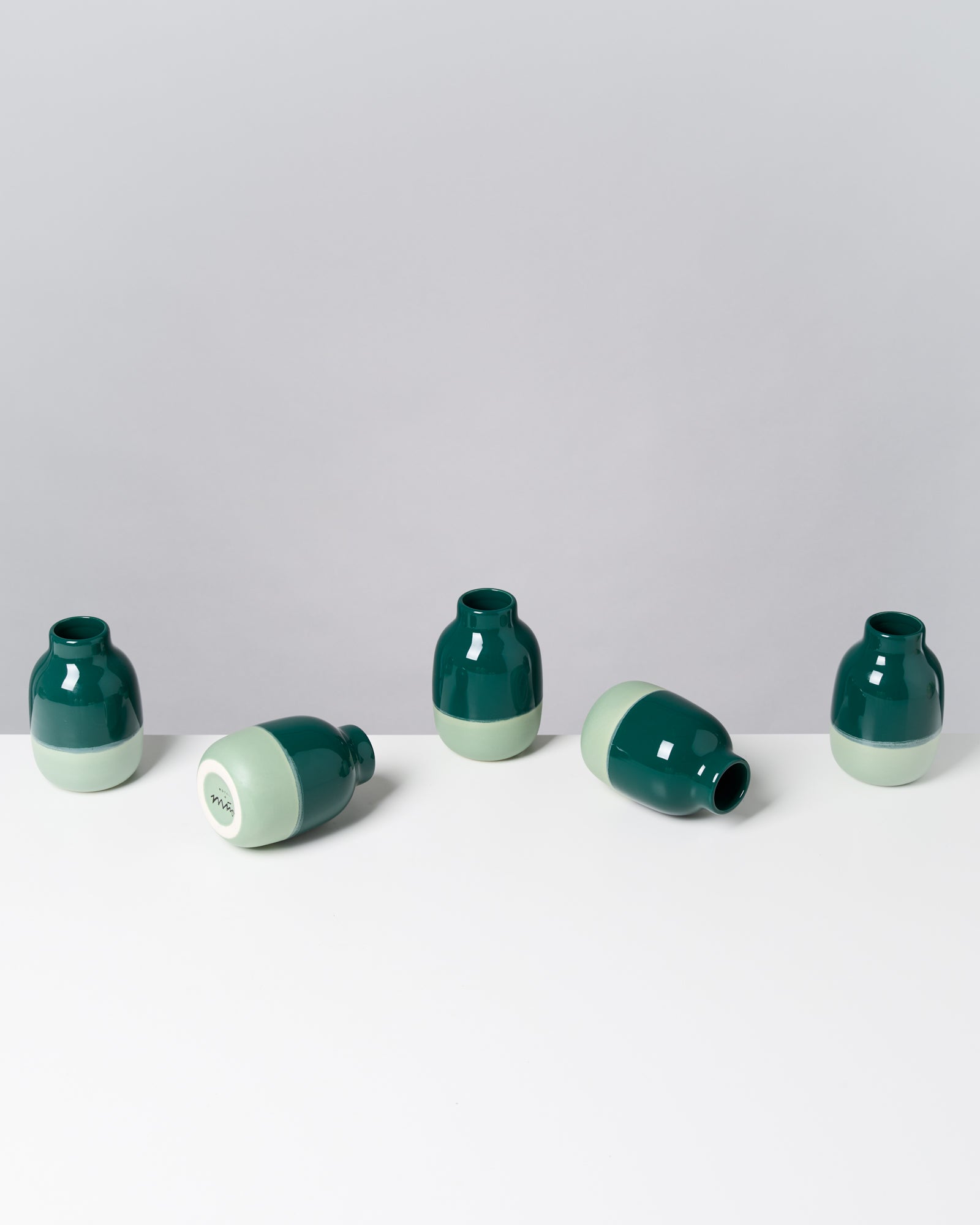 Fünf zweifarbige Vasen in Grün und Mint, drei stehen, zwei liegen auf einer weißen Fläche.