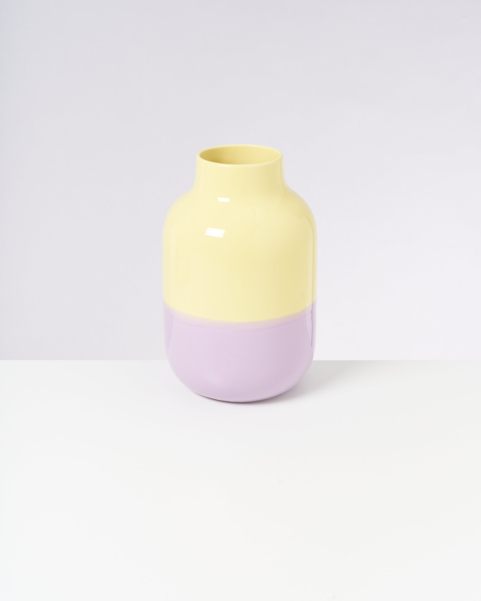 Bunte Vase mit gelbem Oberteil und lila Unterteil auf weißem Hintergrund.