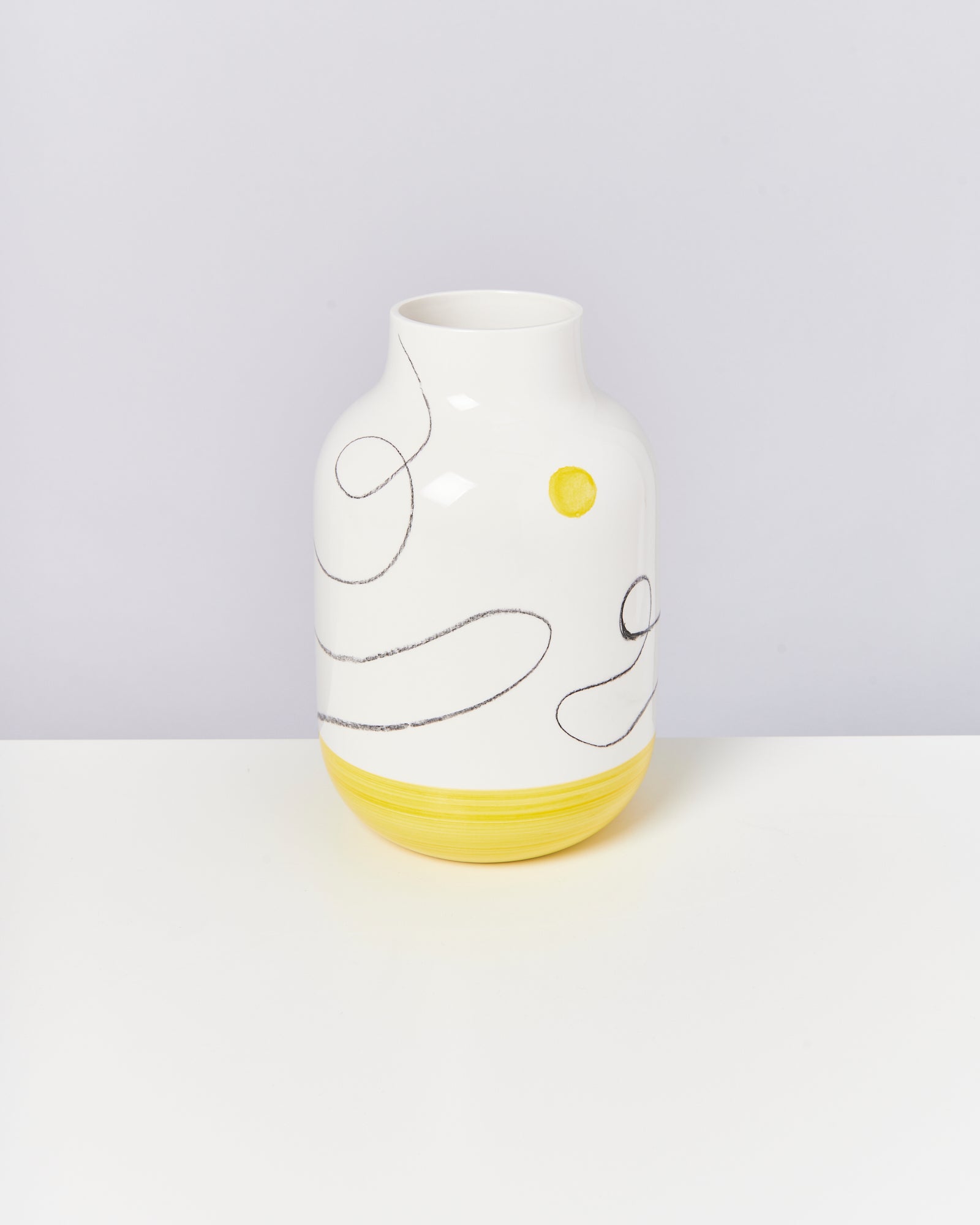 Weiße Vase mit gelben und schwarzen, geschwungenen Linien, steht auf einem weißen Hintergrund.
