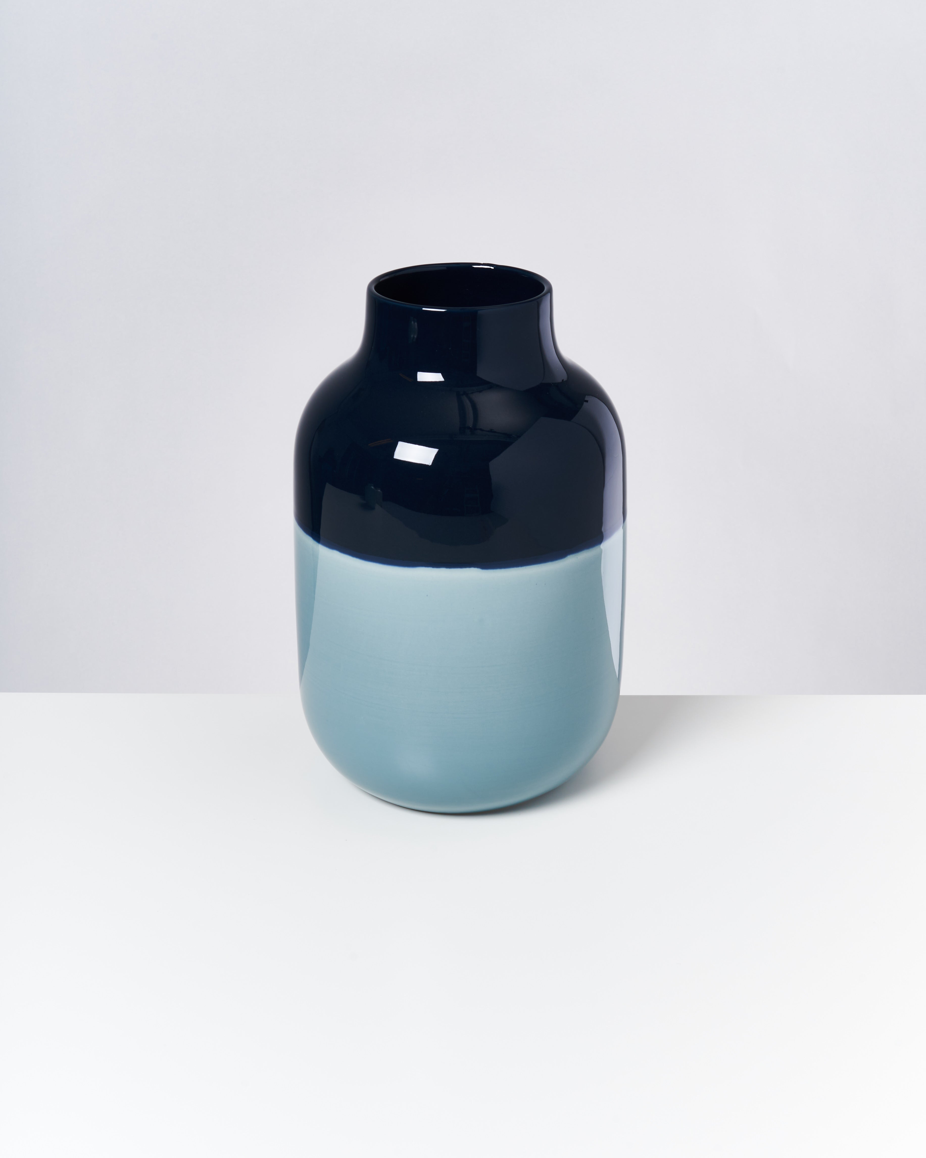 Zweifarbige Vase mit glänzend dunkelblauem oberen Teil und mattem hellblauem unteren Teil auf weißem Hintergrund.