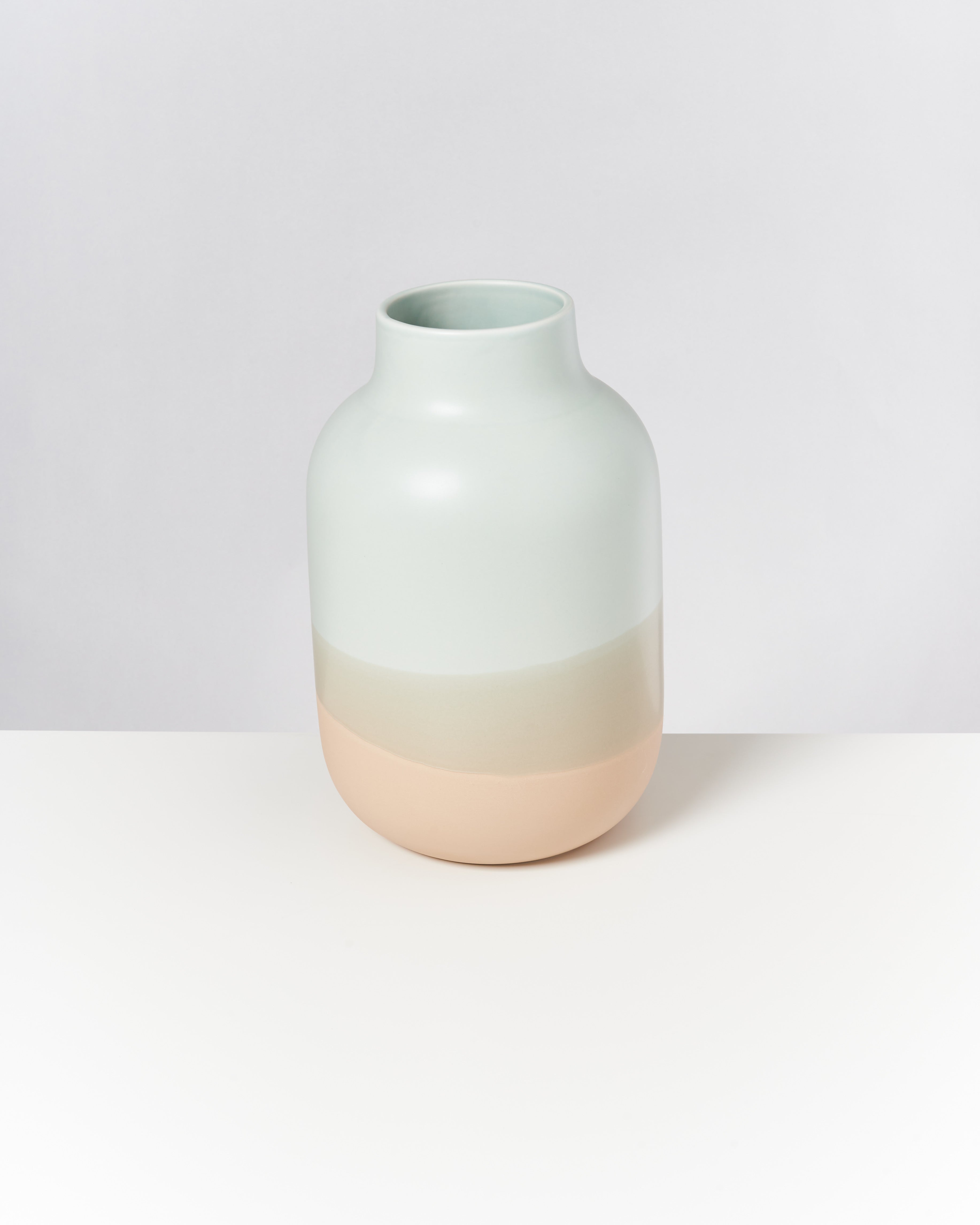 Keramikvase mit abgerundeter Form in Weiß- und Beigetönen auf einer weißen Oberfläche.