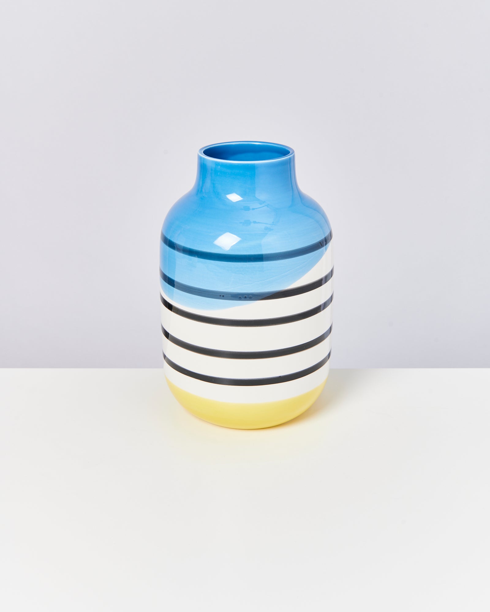 Bunte Vase mit blauen, schwarzen, weißen und gelben Streifen auf einem hellen Hintergrund.