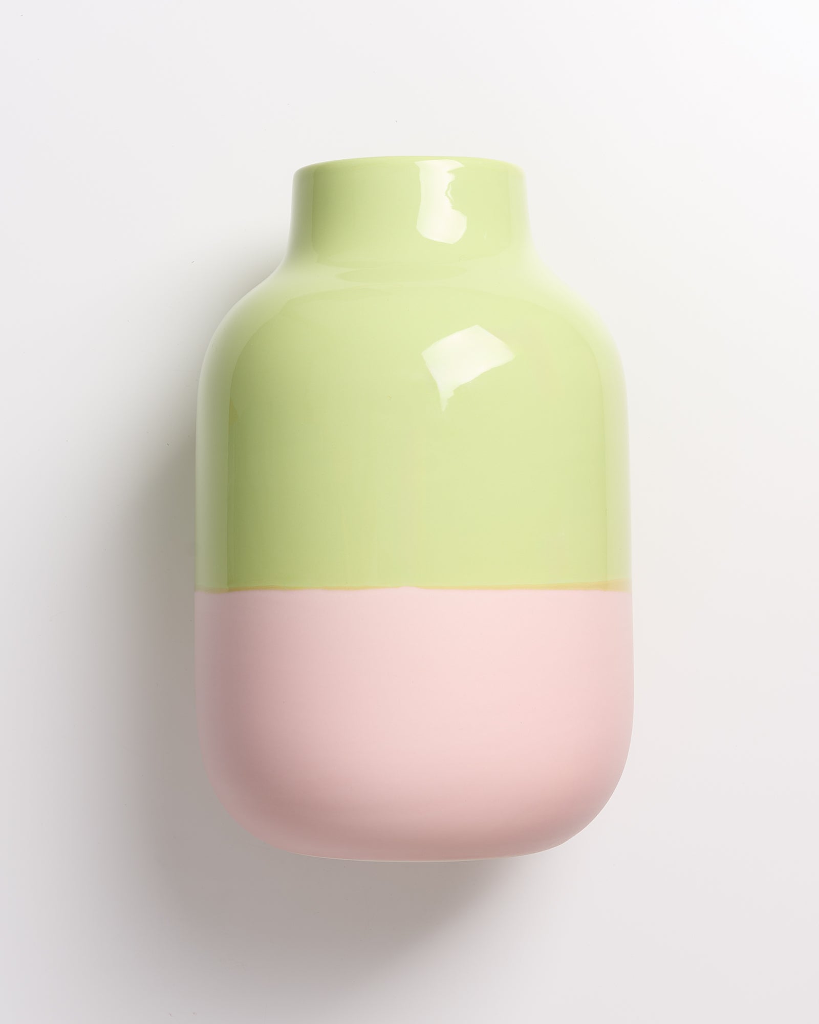 Zweifarbige Vase mit pastellgrünem oberen und rosa unterem Teil auf weißem Hintergrund.