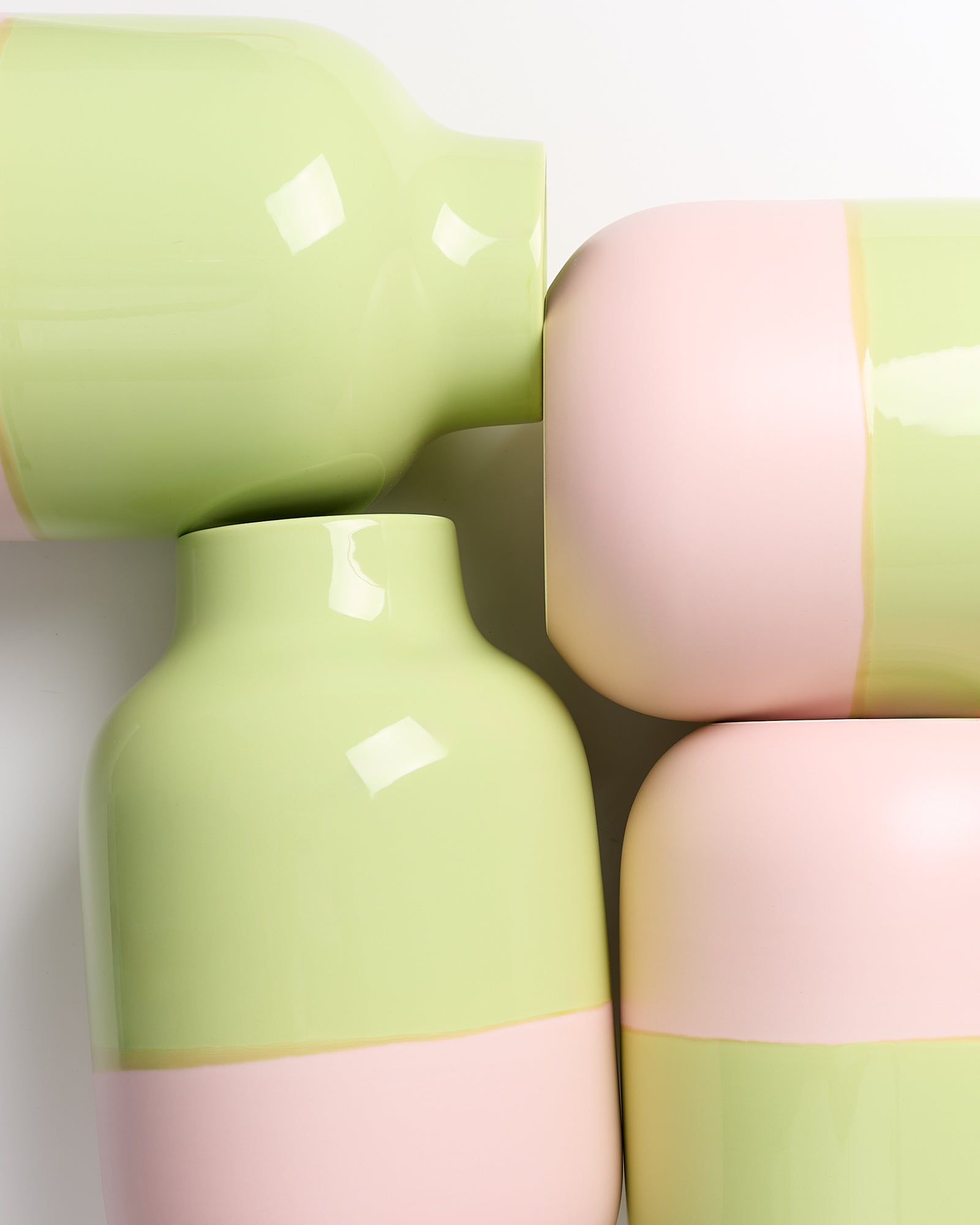 Vier Vasen in Pastellfarben, hellgrün und rosa, stehen und liegen ineinander verschachtelt auf weißem Hintergrund.