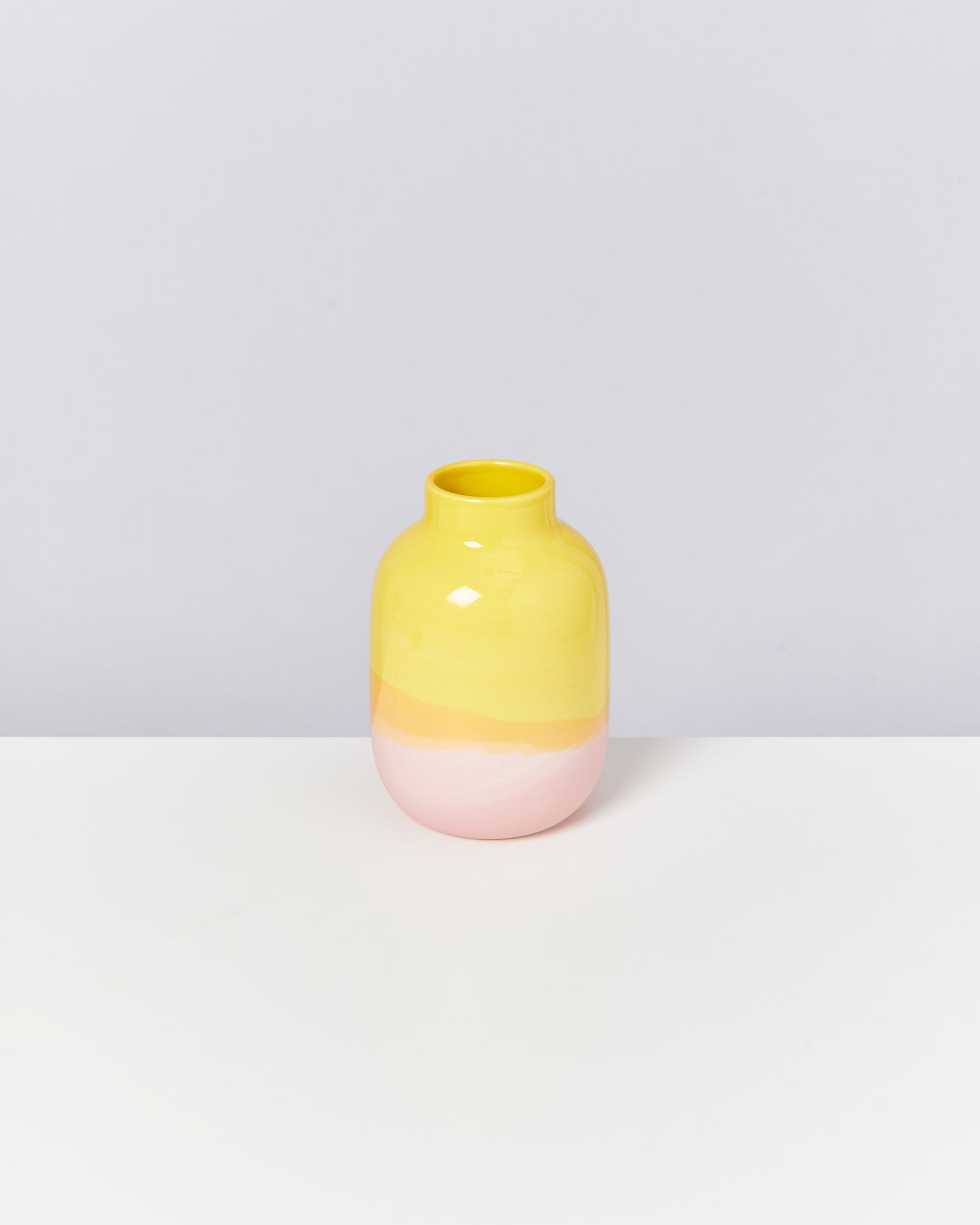 Gelbe, orange und pinke Keramikvase steht auf einem weißen Hintergrund.
