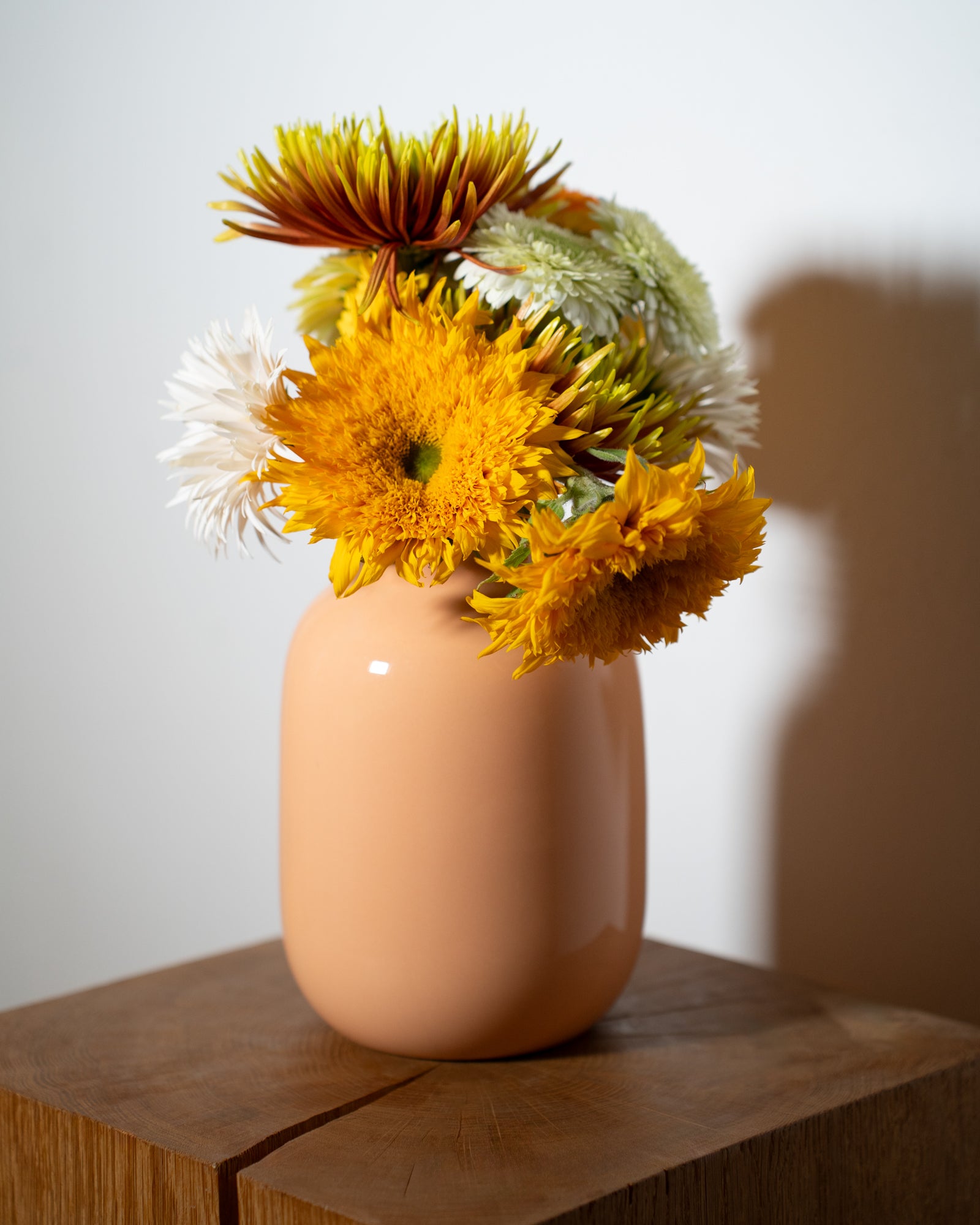 Eine orange Vase mit bunten Blumen steht auf einem Holzwürfel vor einem weißen Hintergrund.