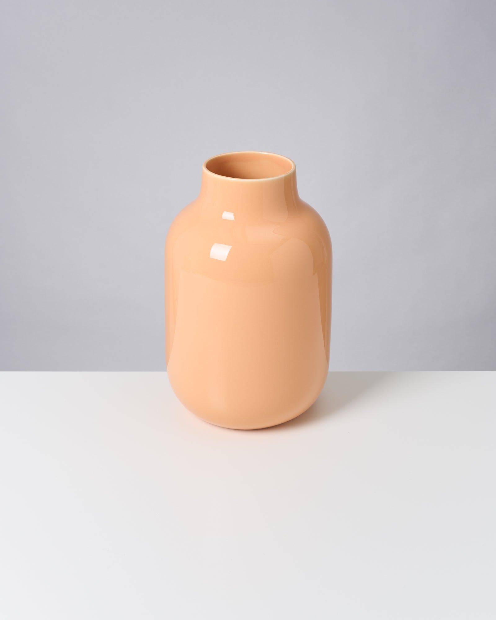 Beige Vase auf weißem Tisch vor grauem Hintergrund.
