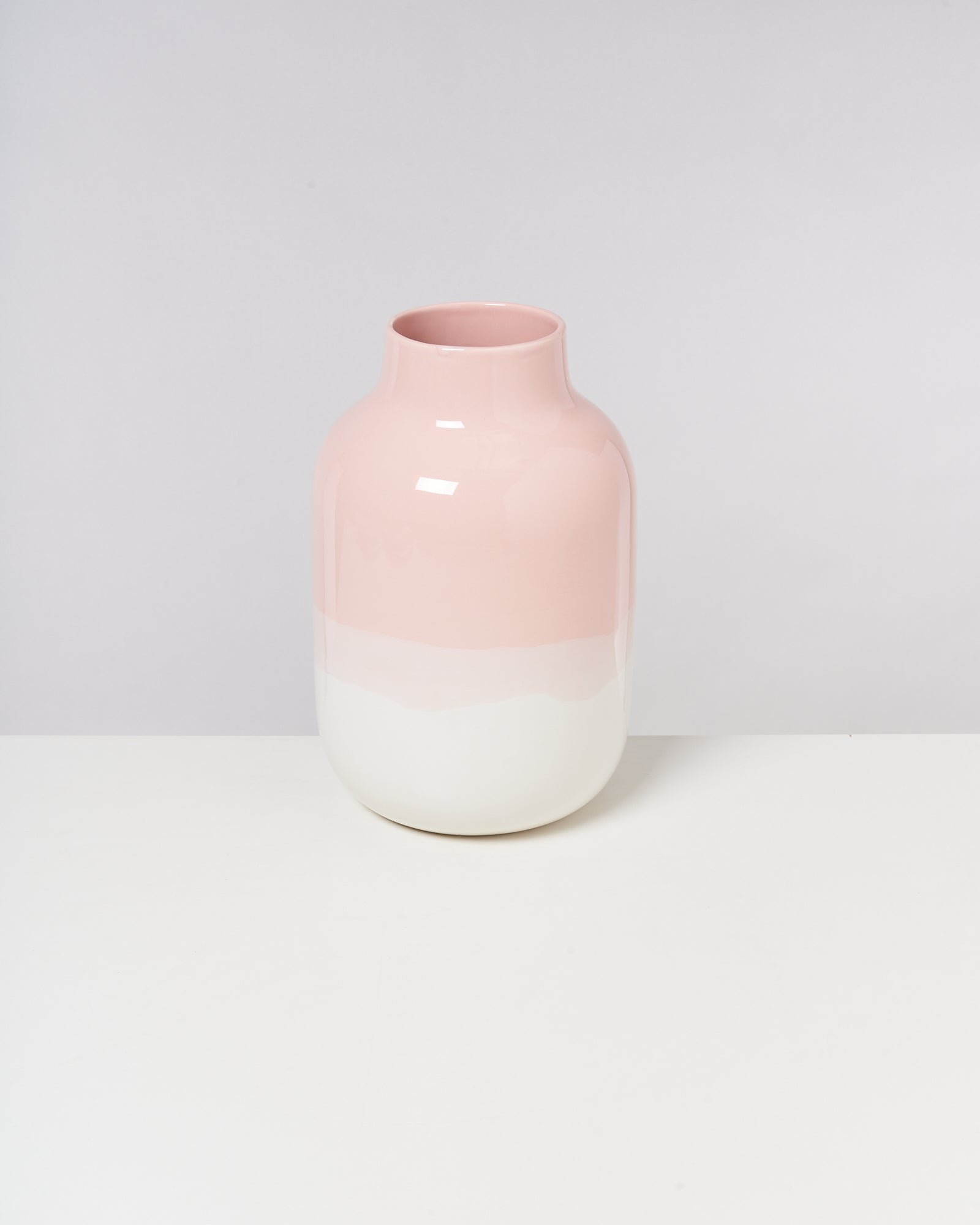 Zweifarbige Vase in Rosa und Weiß auf einem weißen Tisch vor einem grauen Hintergrund.
