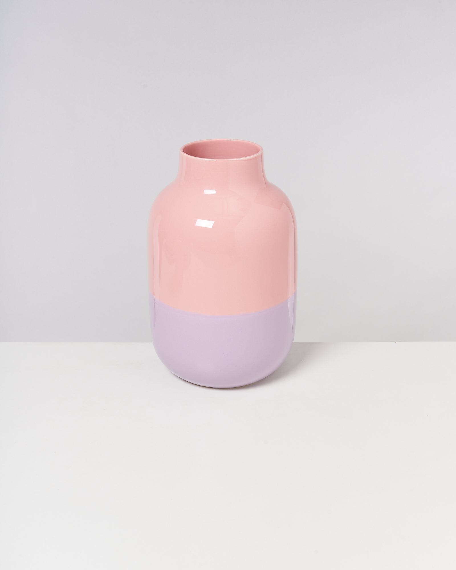 Rosa-lila Vase vor einem grauen Hintergrund auf einem weißen Tisch.
