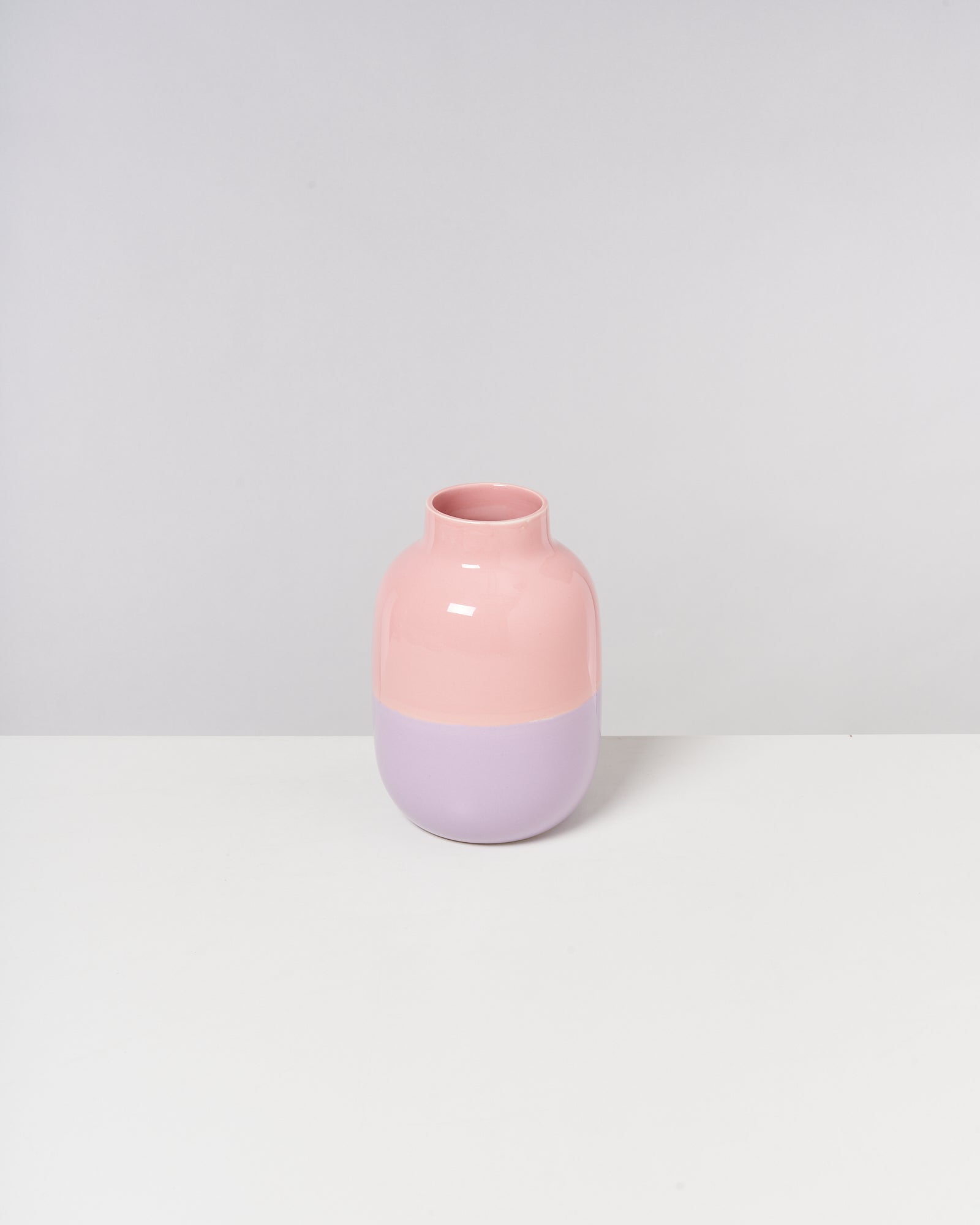 Eine zweifarbige Vase in Rosa und Lila steht auf einem weißen Hintergrund.