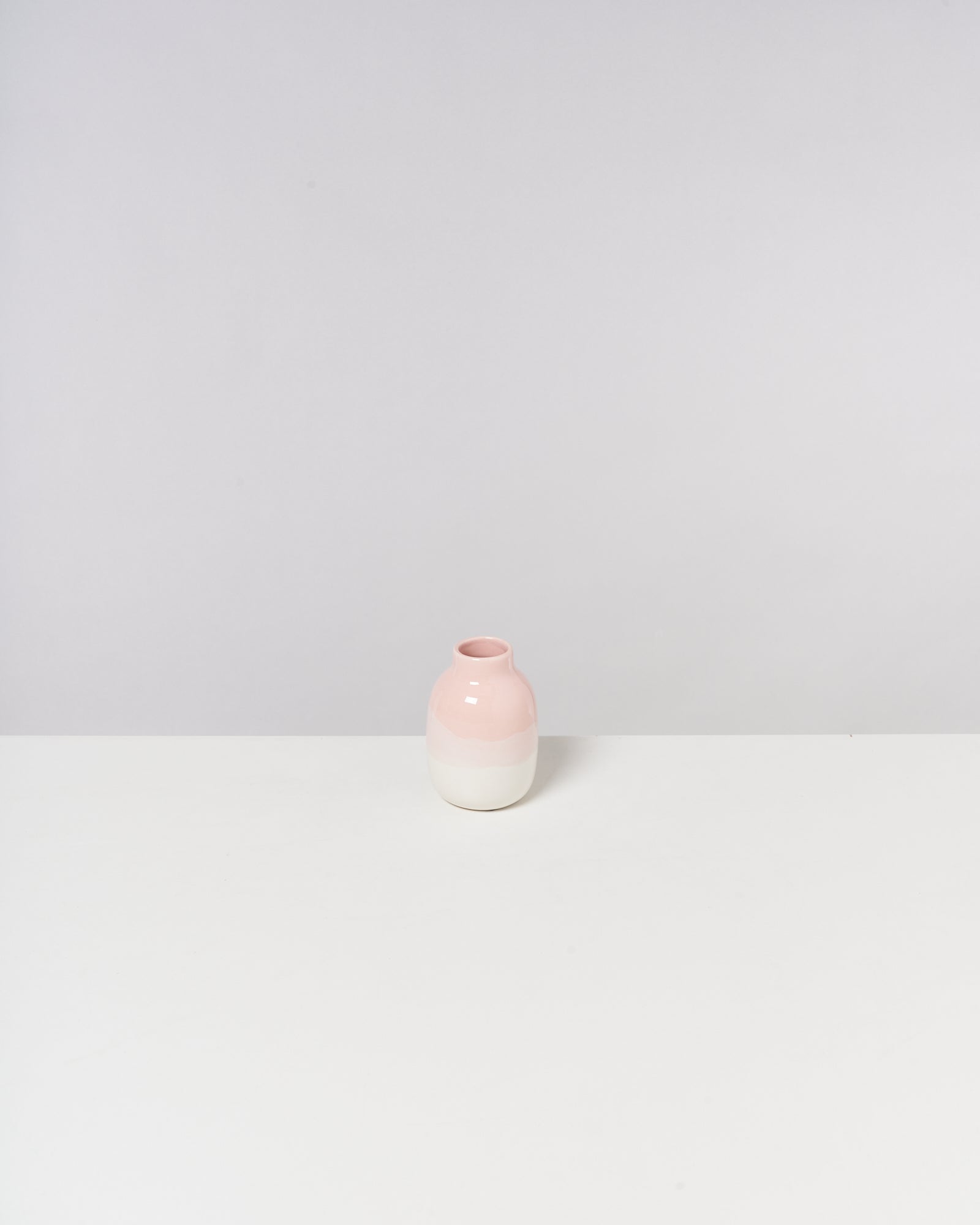 Eine runde Vase in Rosa und Weiß steht auf einem weißen Tisch vor einem hellgrauen Hintergrund.