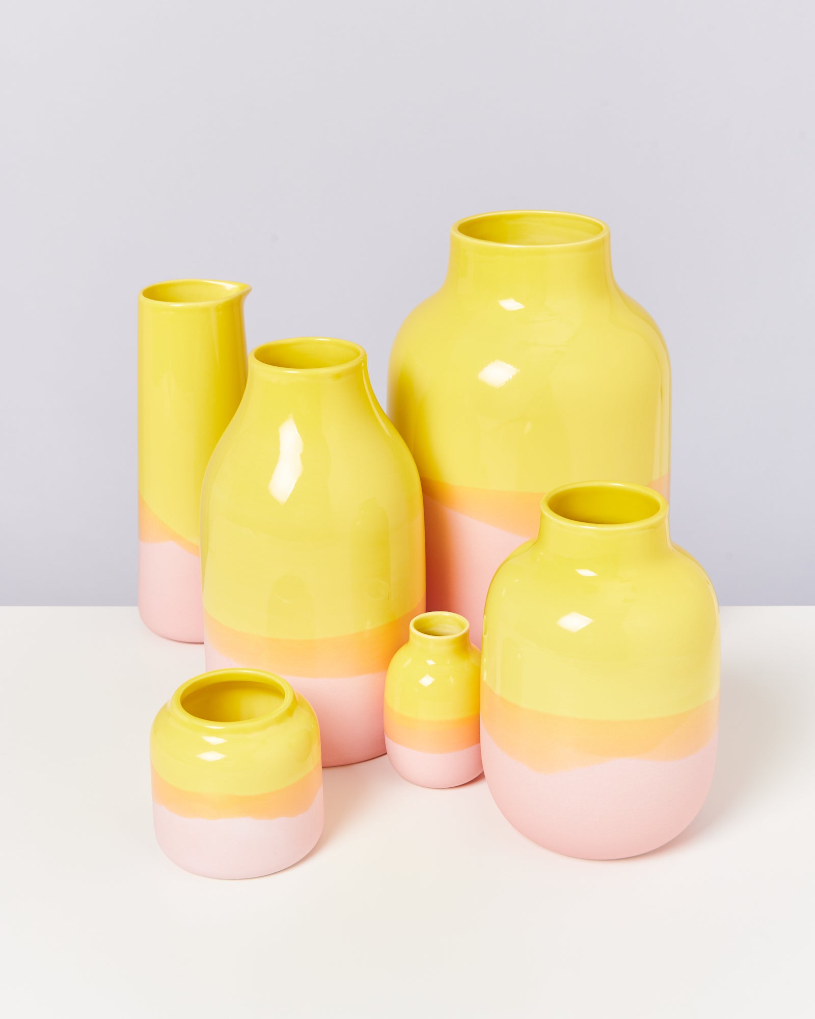 Sechs bunte Keramikkrüge in Gelb, Orange und Rosa auf weißem Hintergrund.