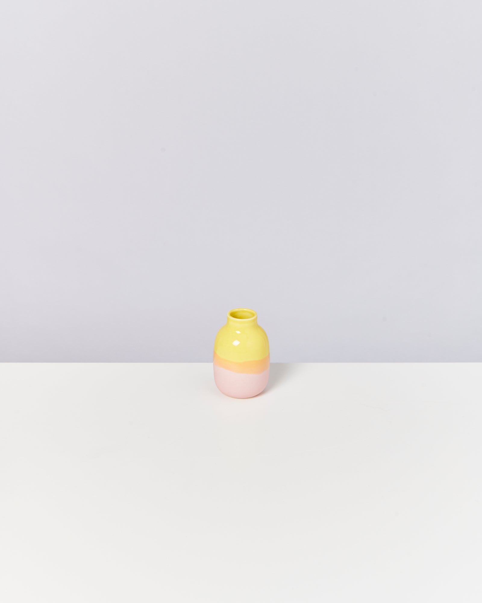 Gelbe und rosa Vase auf weißem Tisch vor grauem Hintergrund.