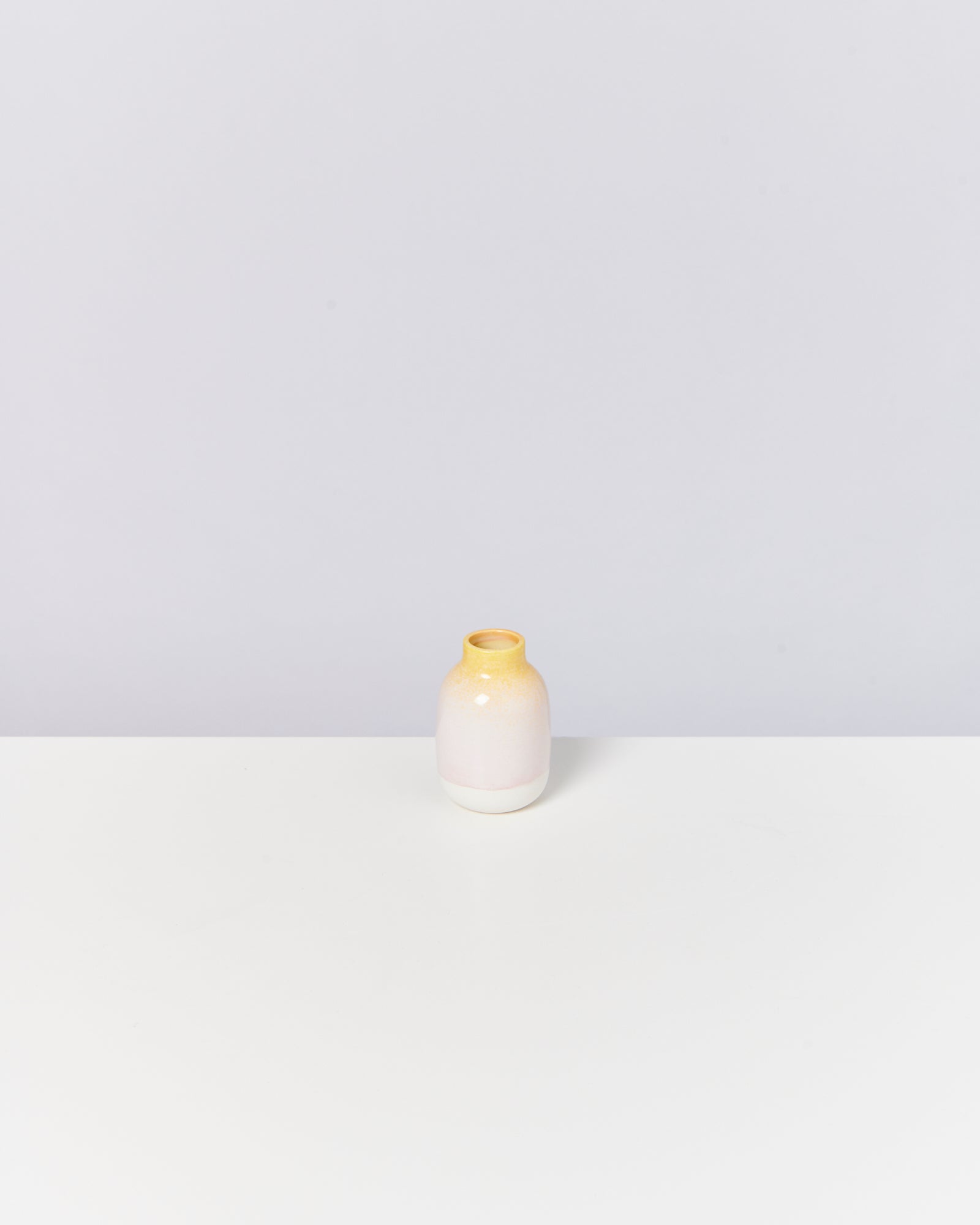 Kleine, gelb-weiß-rosa Vase auf einem weißen Tisch vor grauem Hintergrund.