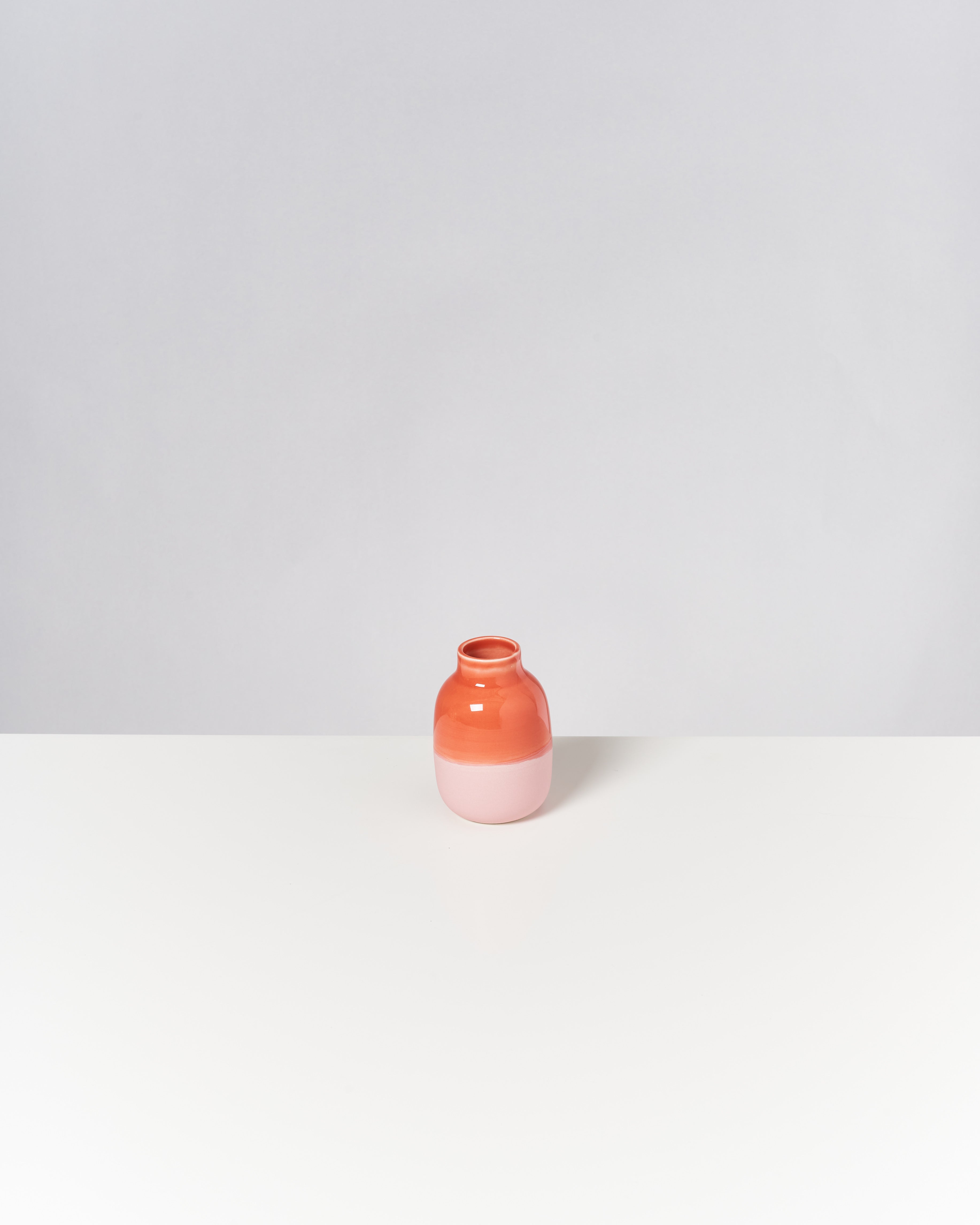 Ein kleiner, zweifarbiger Topf in Rot und Rosa auf einem weißen Tisch vor grauem Hintergrund.