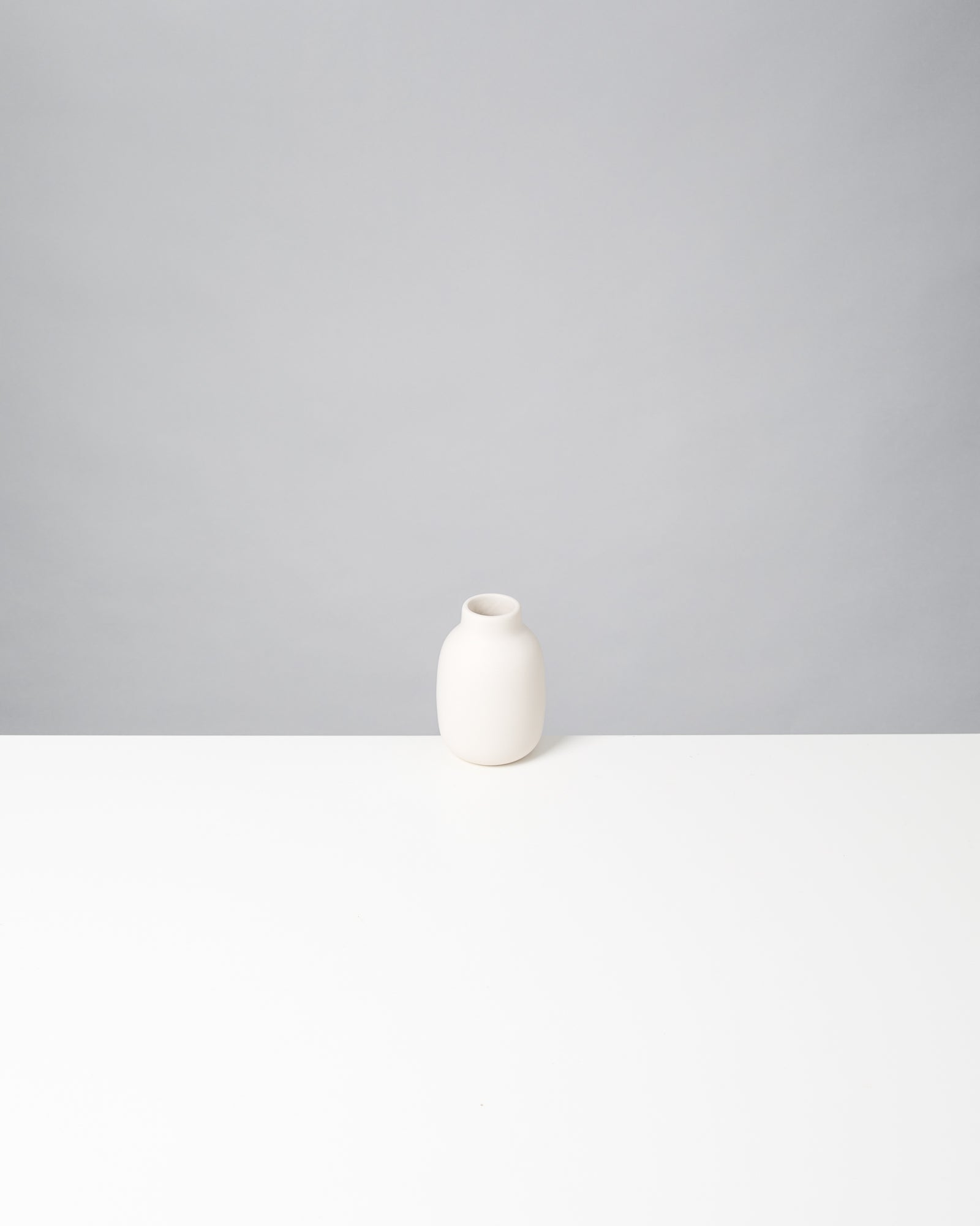 Weiße Vase auf einem weißen Tisch vor grauem Hintergrund.