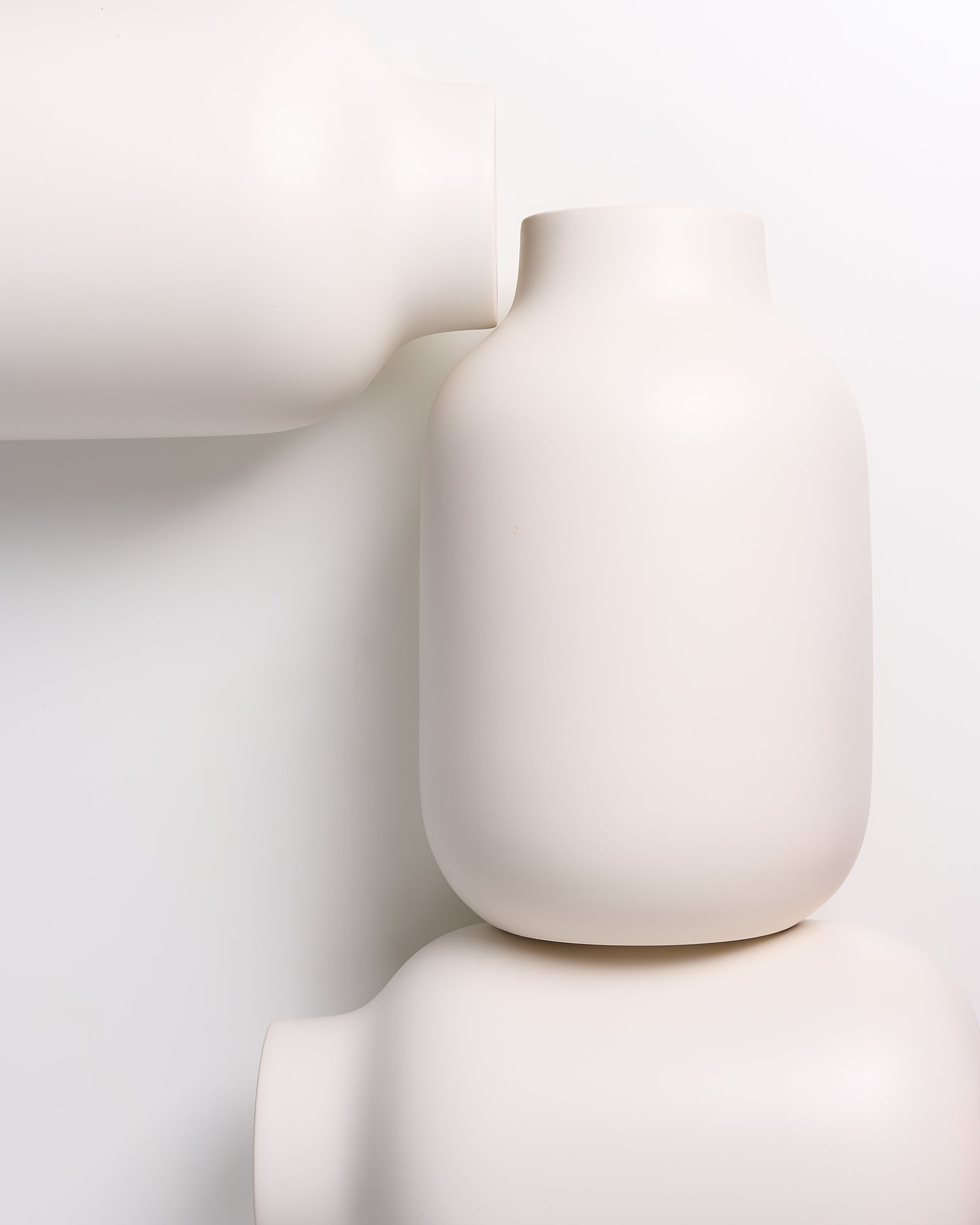 Drei weiße, minimalistische Vasen in verschiedenen Ausrichtungen auf weißem Hintergrund angeordnet.