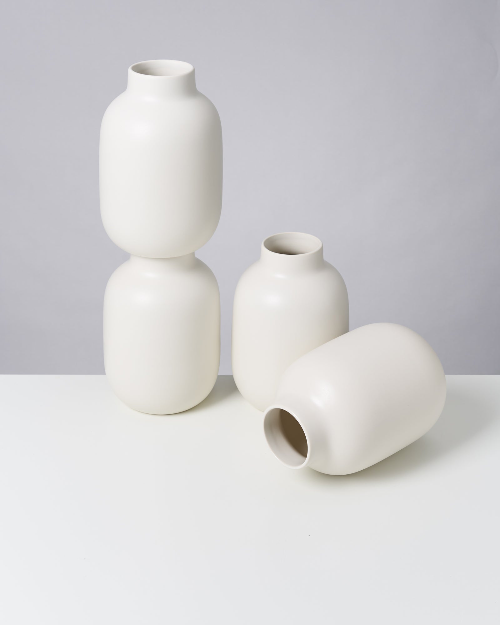 Vier weiße, minimalistische Vasen auf einem weißen Untergrund, eine Vase liegt seitlich.