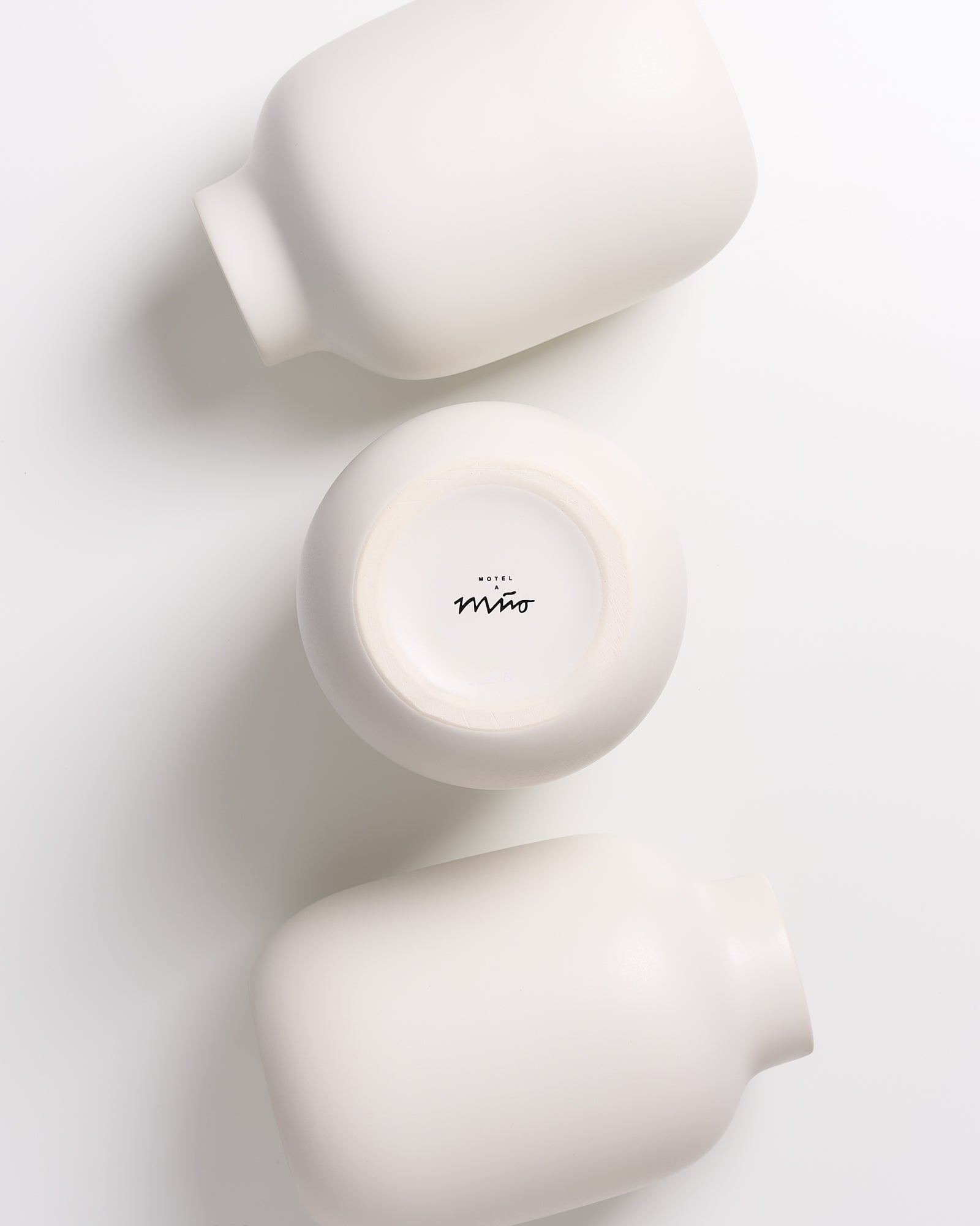 Drei weiße Keramikvasen auf einem weißen Untergrund, eine zeigt den Schriftzug "Hotel Miro" am Boden.