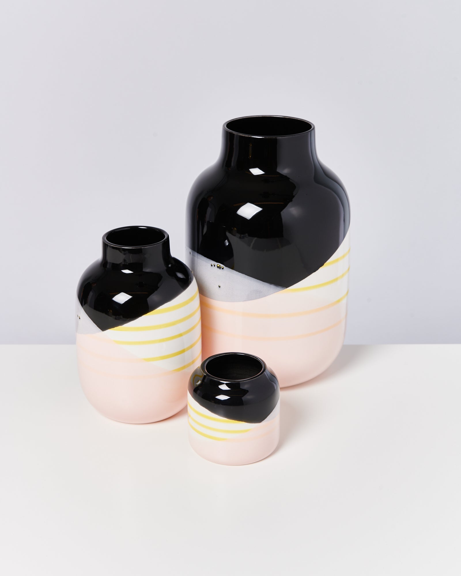 Drei dekorative Vasen in Schwarz, Rosa und Gelb stehen auf einem weißen Untergrund.