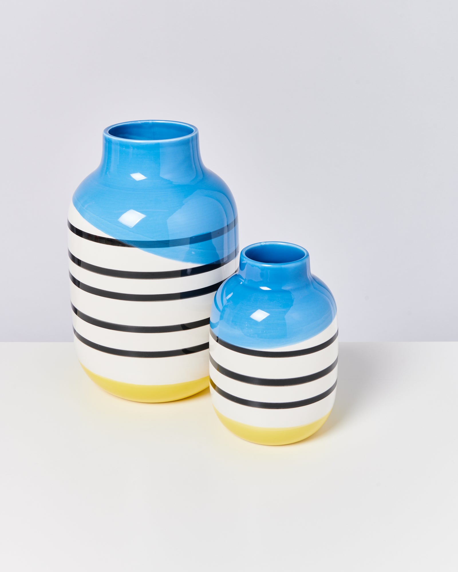 Zwei Vasen mit blauen, weißen und schwarzen Streifen, die auf einem weißen Tisch stehen.