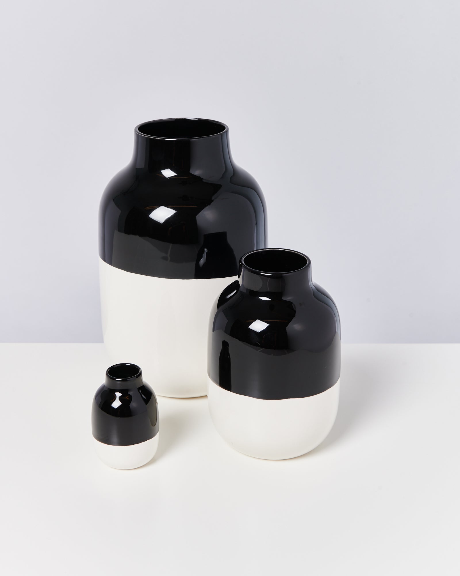 Drei schwarz-weiße Vasen in unterschiedlichen Größen stehen auf einer weißen Oberfläche vor einem grauen Hintergrund.
